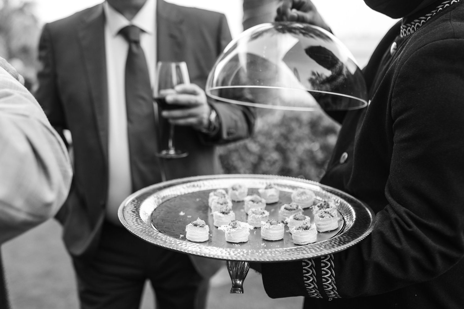 Black and white detail shot of champagne being served on elegant silver trays.