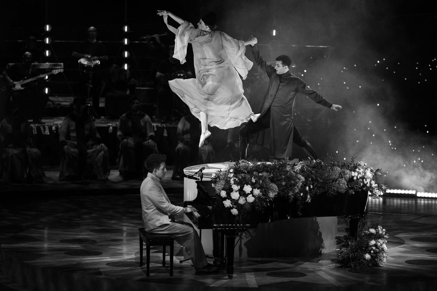 Black and white performance shot showing musicians on stage with dramatic lighting.