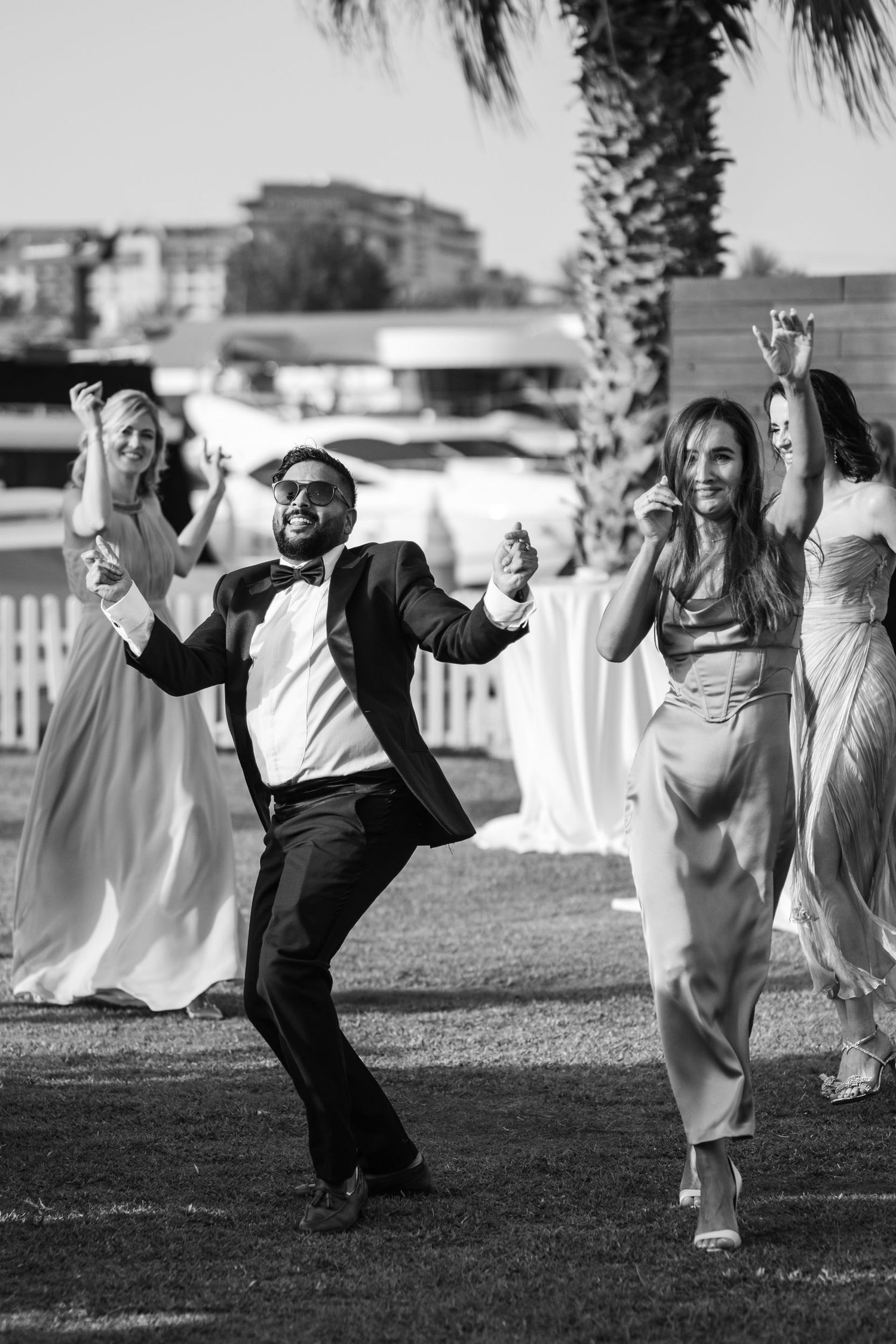 Wedding party members dancing and celebrating on grass lawn.