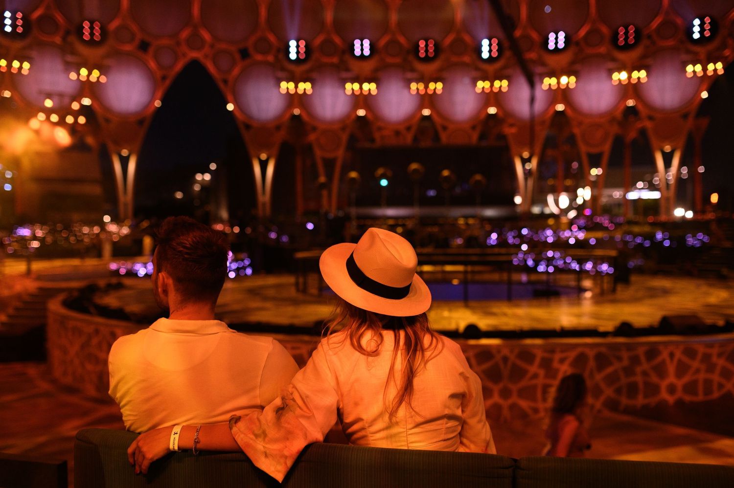 Evening outdoor venue with warm lighting and decorative string lights overhead.