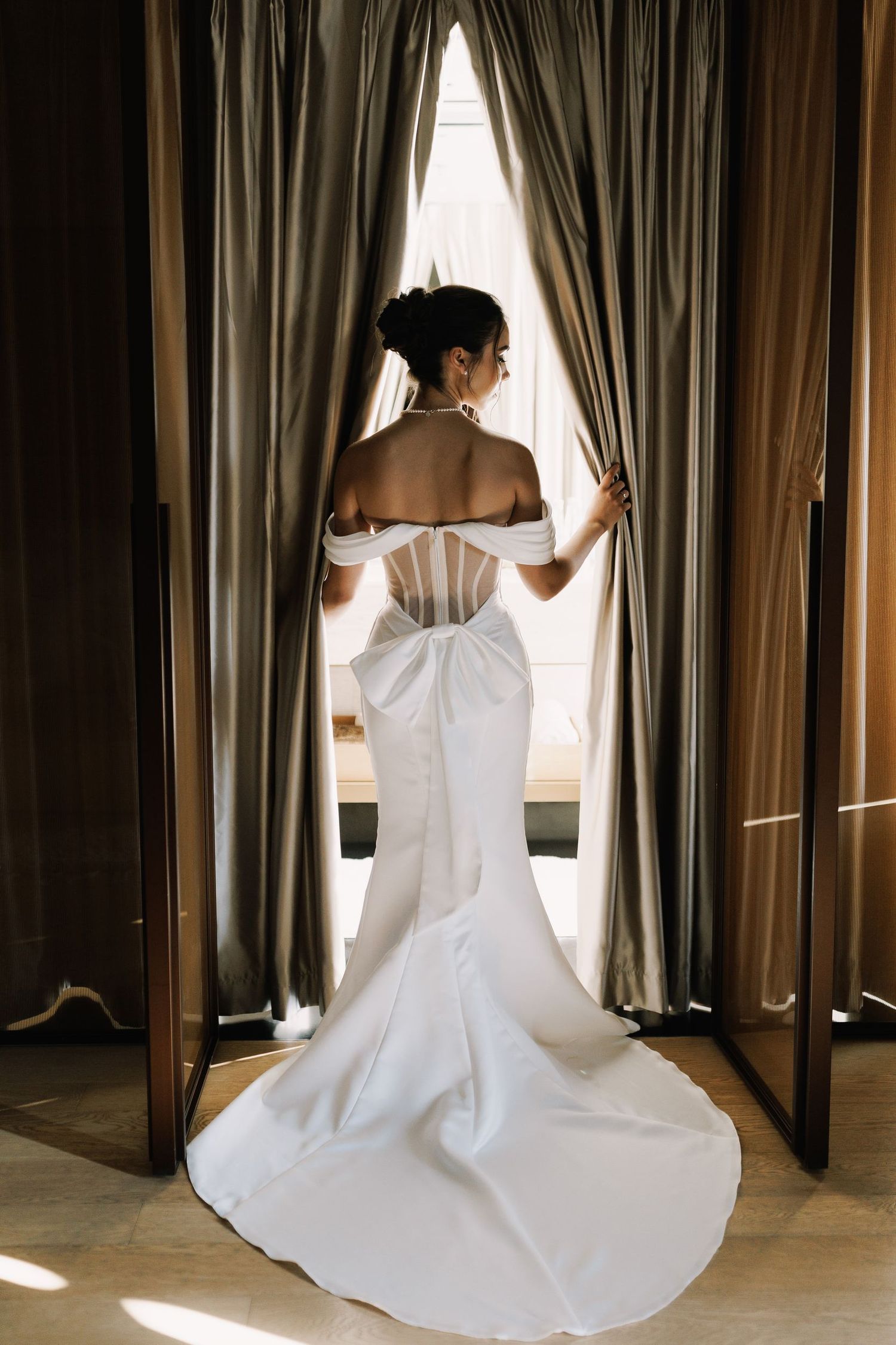 Back view of a white mermaid wedding dress with dramatic train by curtained windows.