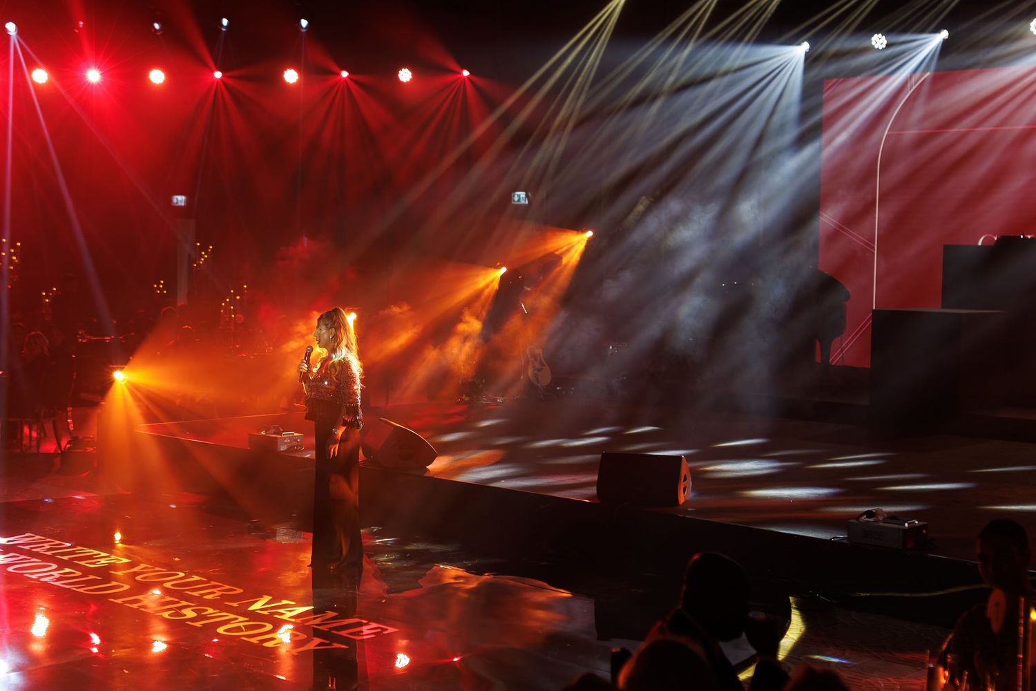 Wide shot of a concert stage bathed in red spotlights and atmospheric effects.