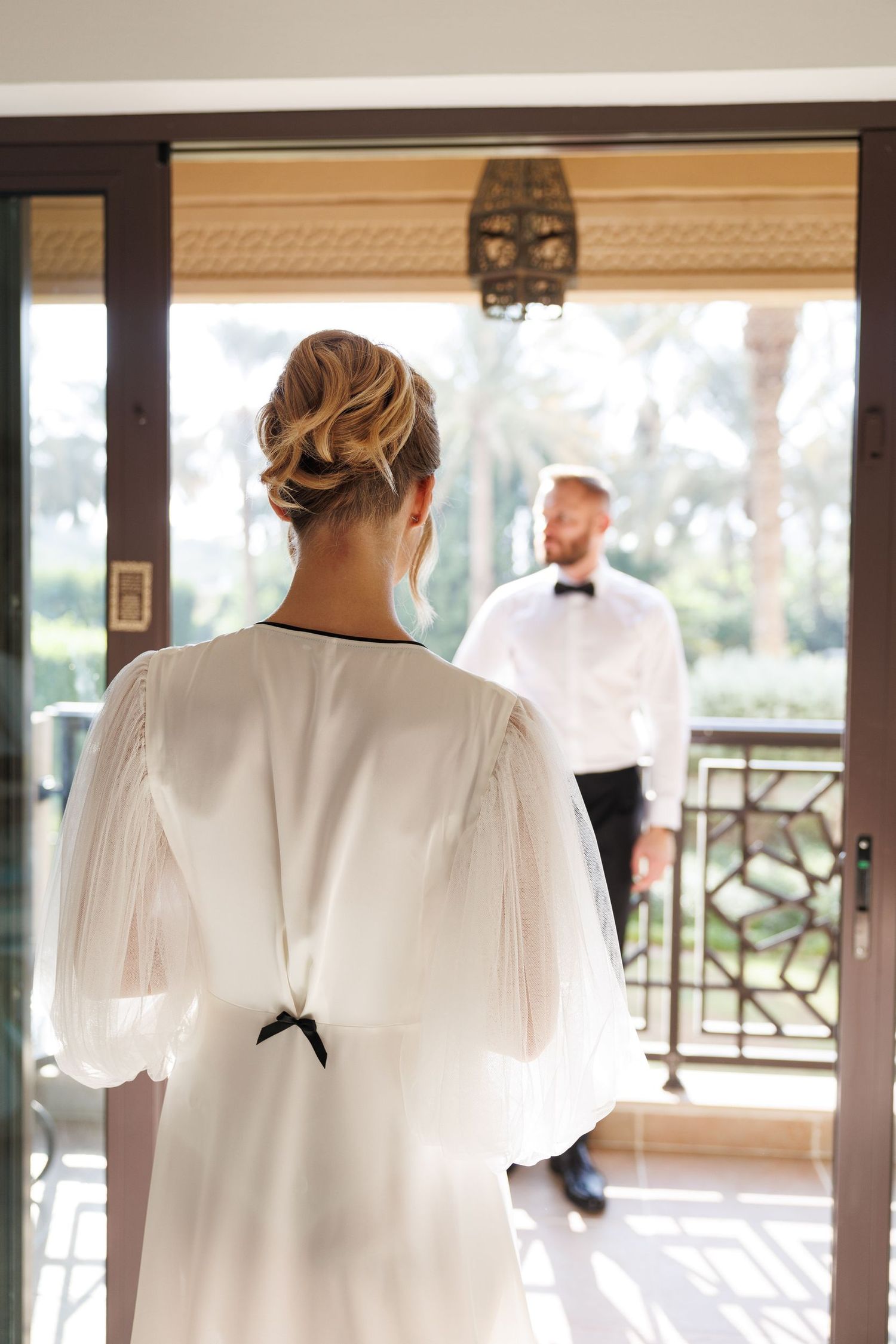 White wedding dress hanging in doorway with natural light streaming through windows.