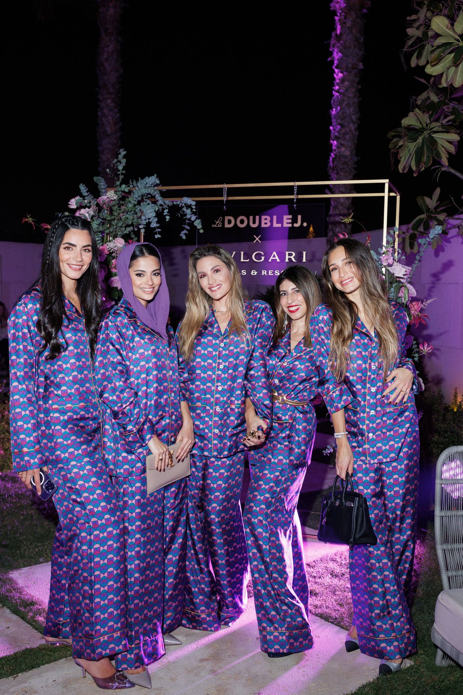 Group in matching blue patterned outfits pose together at nighttime event with purple lighting.
