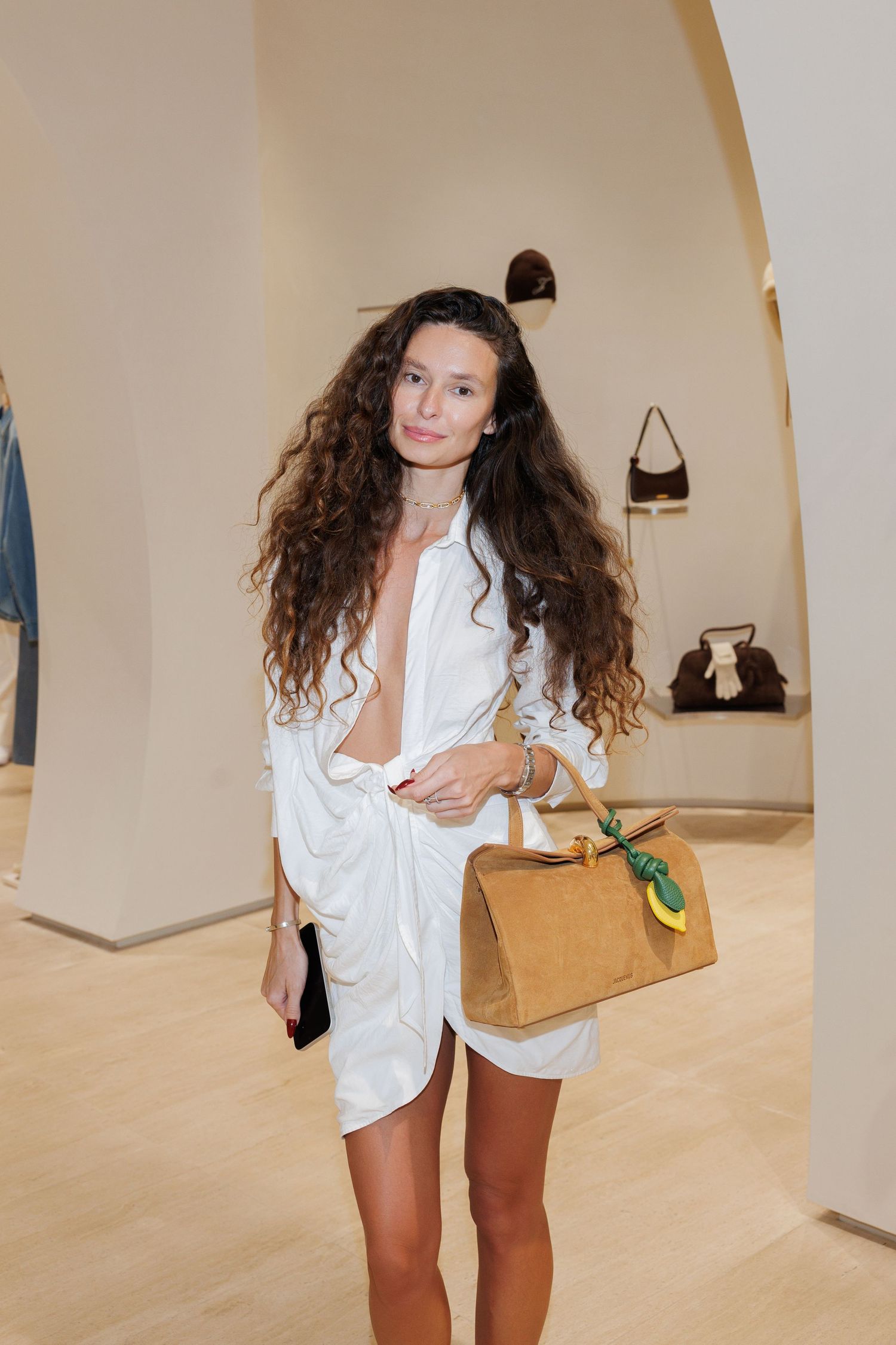 Person in white outfit posing with handbag in a bright gallery space.