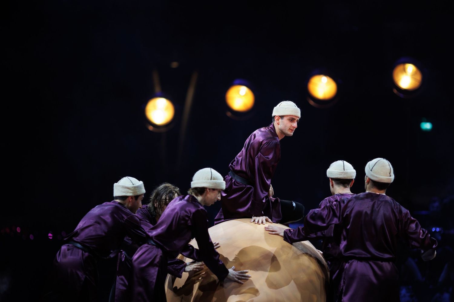 Group performance showing acrobatic moves with performers in purple costumes on stage.