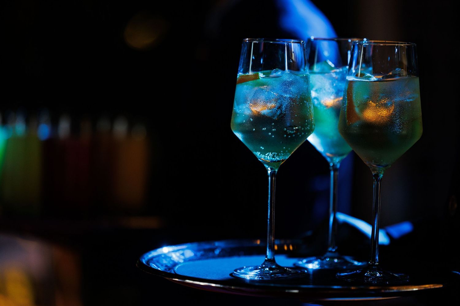Blue-lit cocktail glasses arranged on a dark surface creating an elegant ambiance.