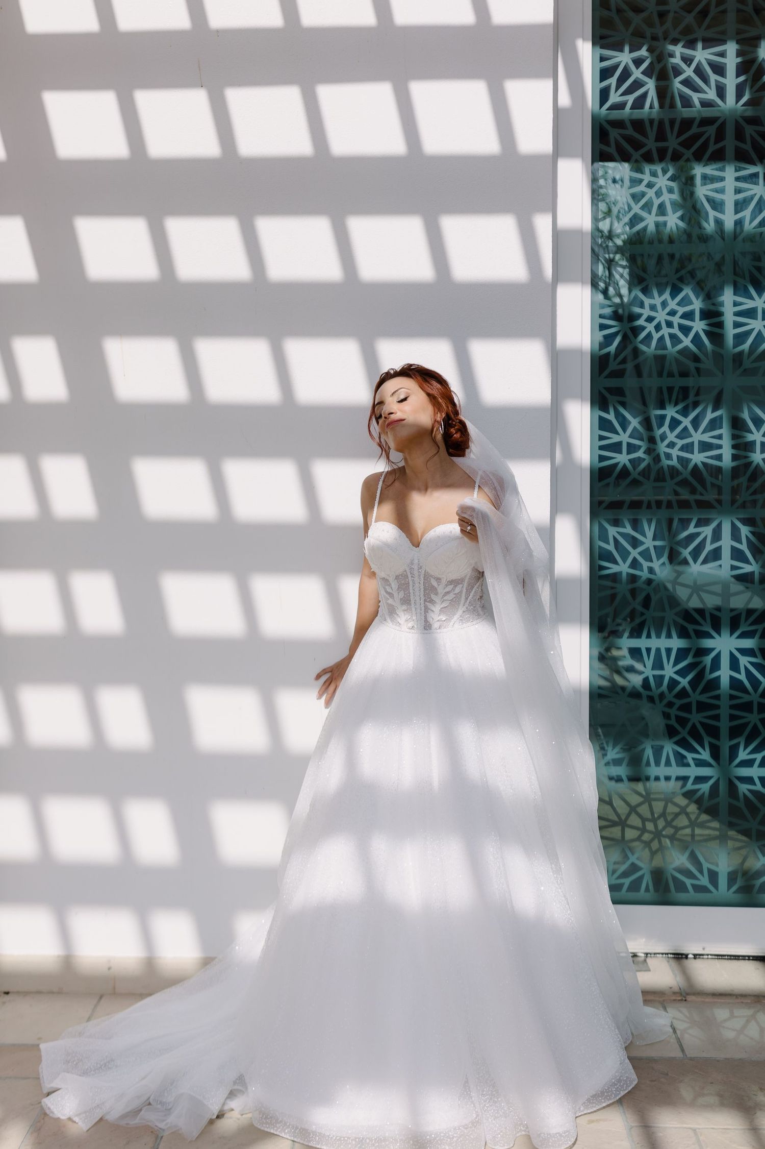 A white wedding gown creates dramatic shadows against a geometric patterned wall.