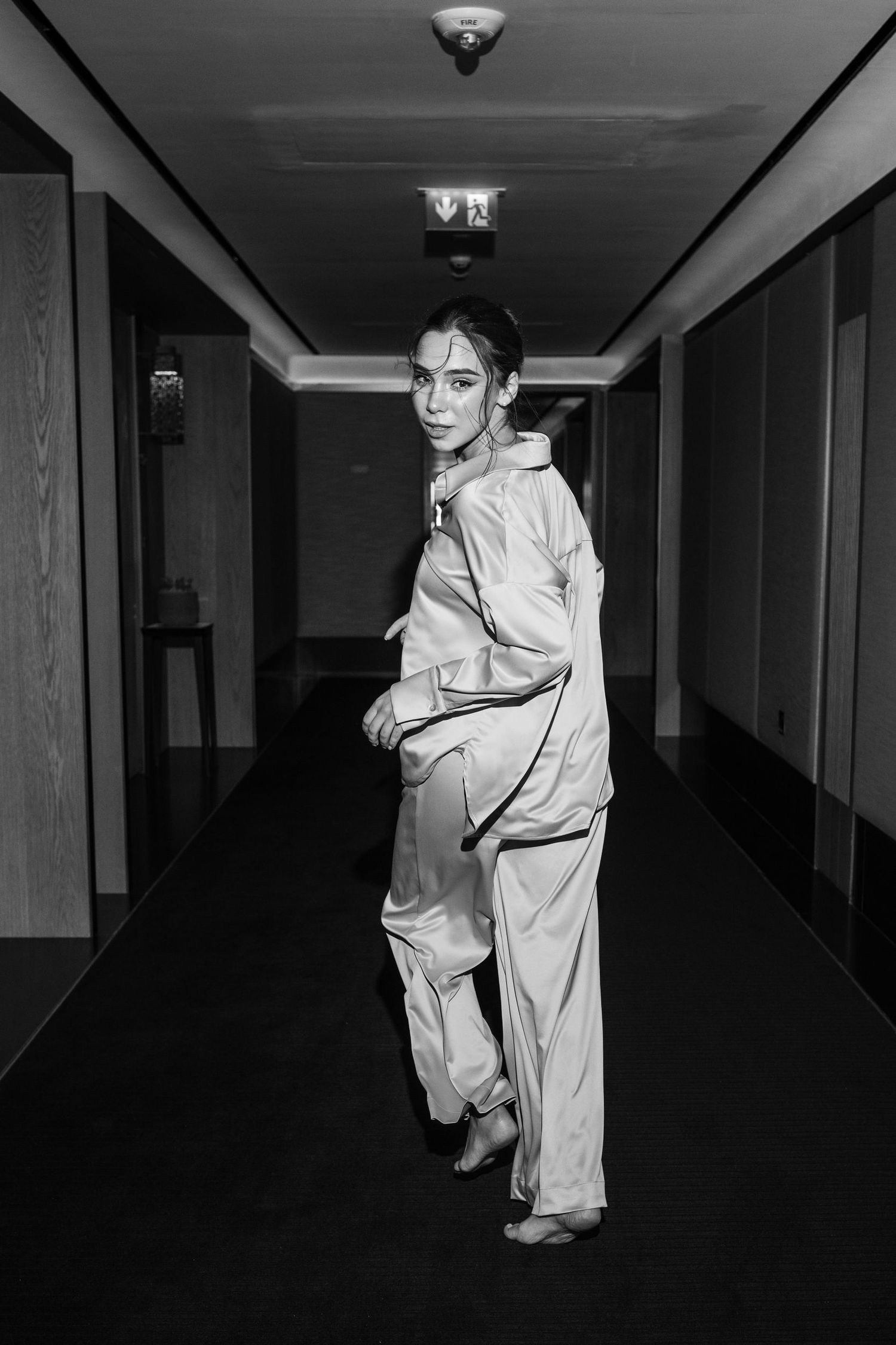 Black and white fashion portrait in hotel hallway wearing oversized light colored outfit.
