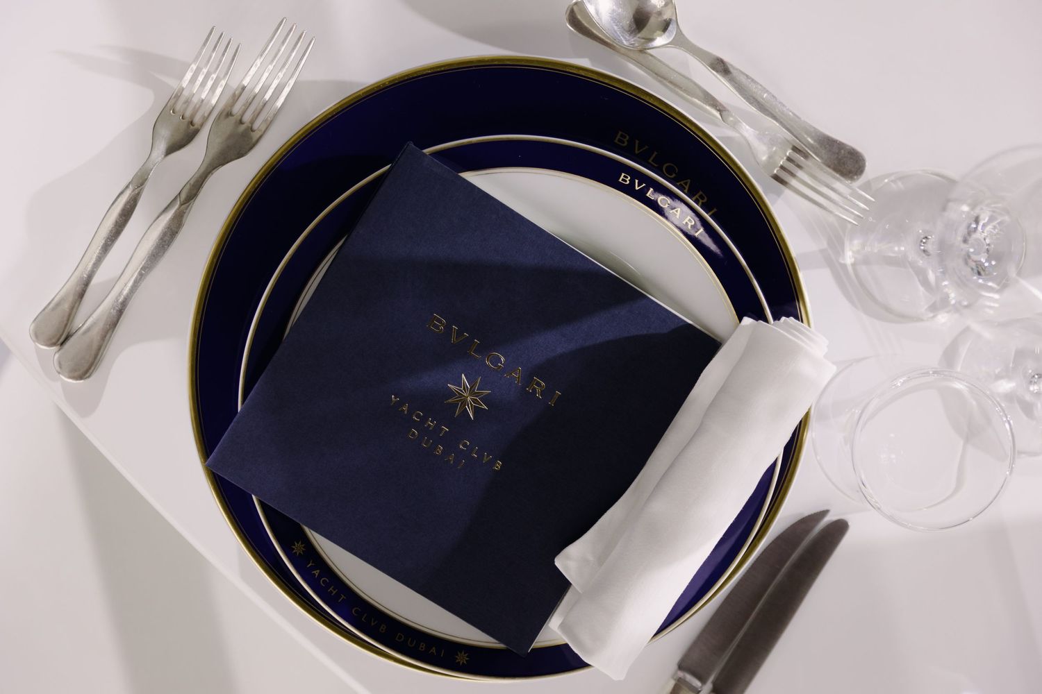 Formal place setting with navy blue accents and elegant silverware on white tablecloth.