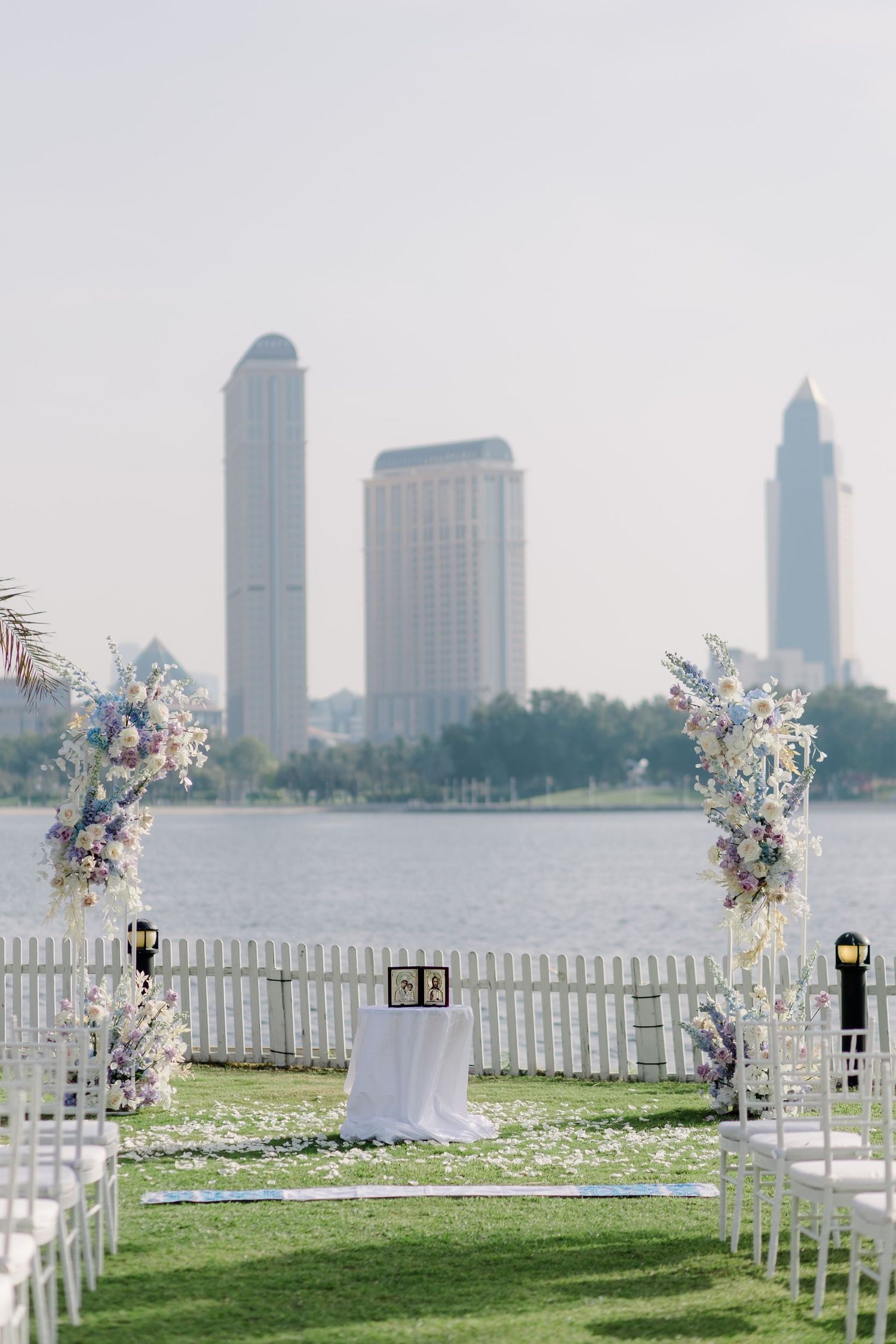 Wedding ceremony setup with white chairs and floral arrangements against a city skyline backdrop.