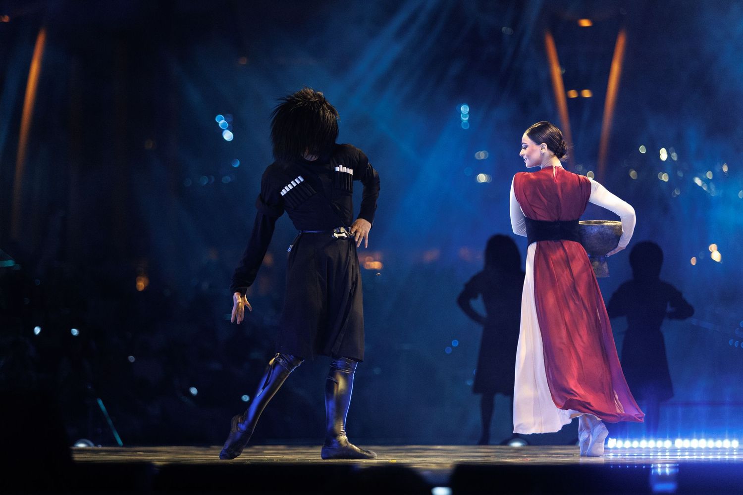 Performers dancing under intense blue stage lighting creating silhouettes against a dramatic backdrop.