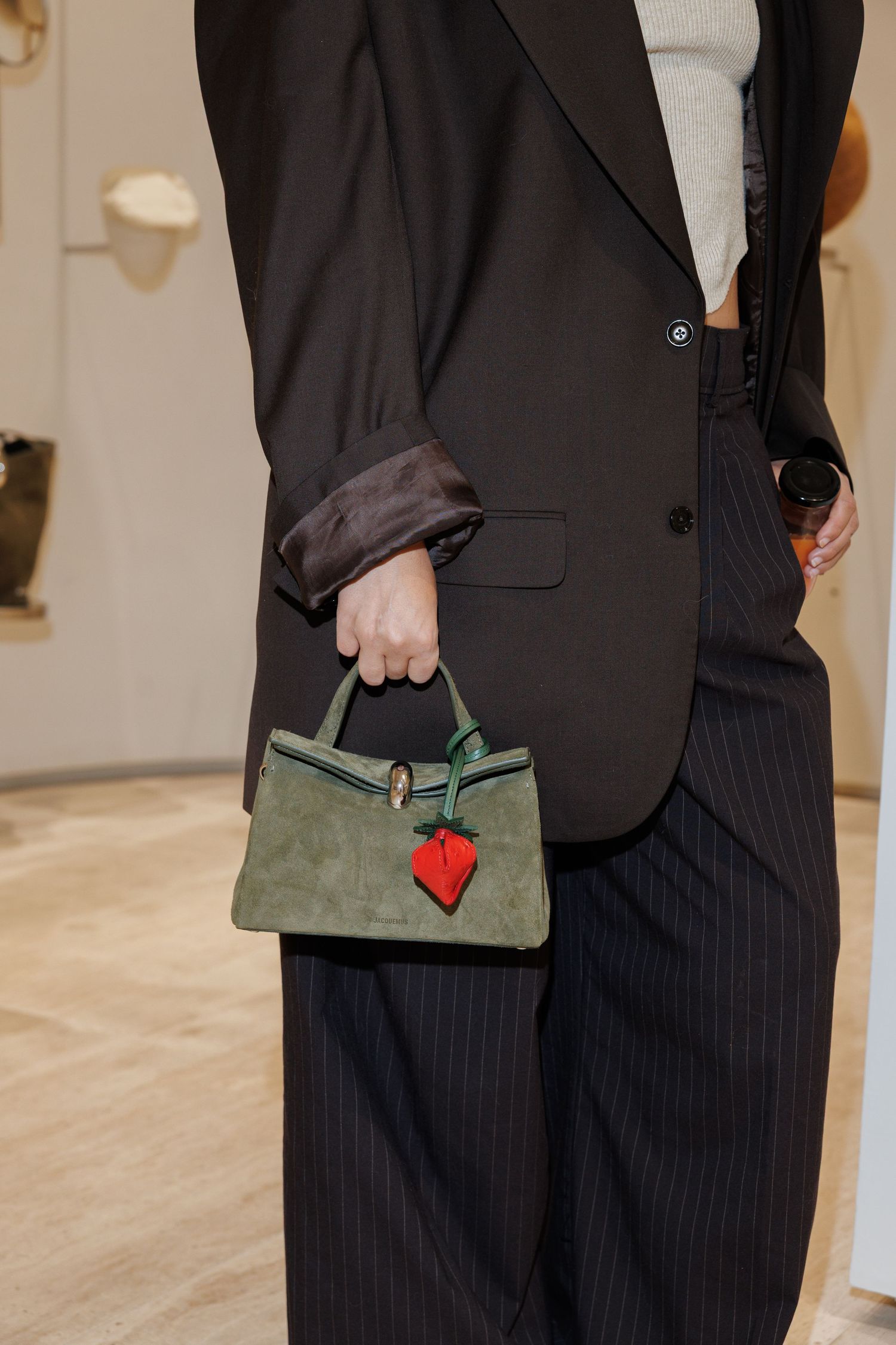 Person in black pinstripe suit holding a green handbag with red detail.