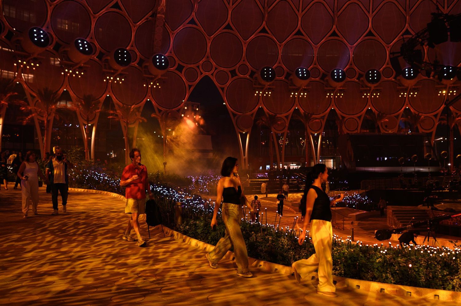 People walking through an illuminated outdoor venue at night.