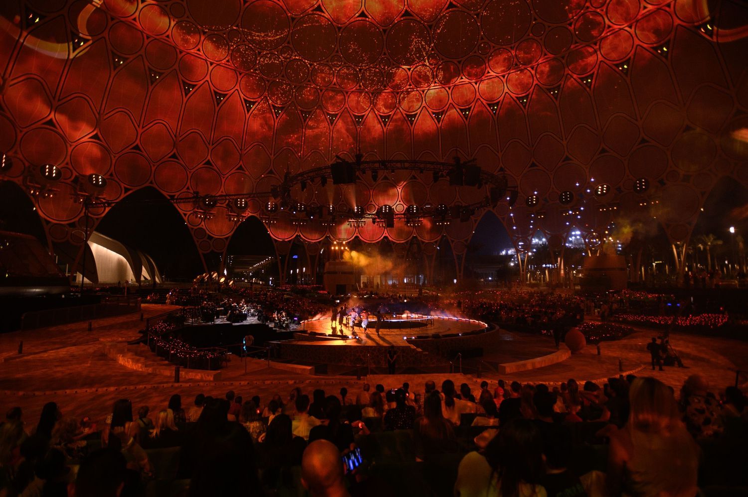 Stadium arena lit in dramatic red lighting during an ice skating performance.