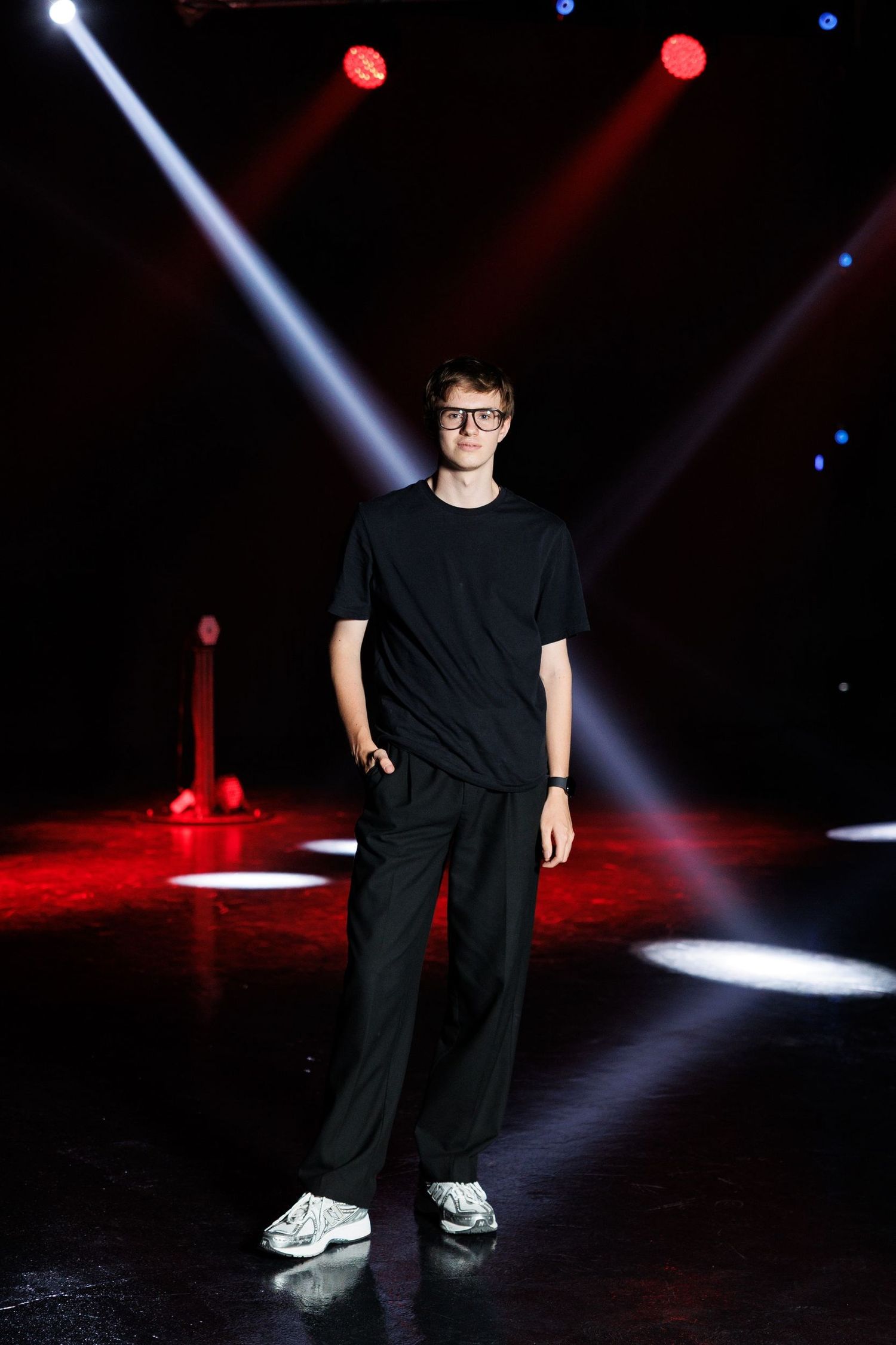 Person in black outfit performing on dark stage with dramatic spotlights.