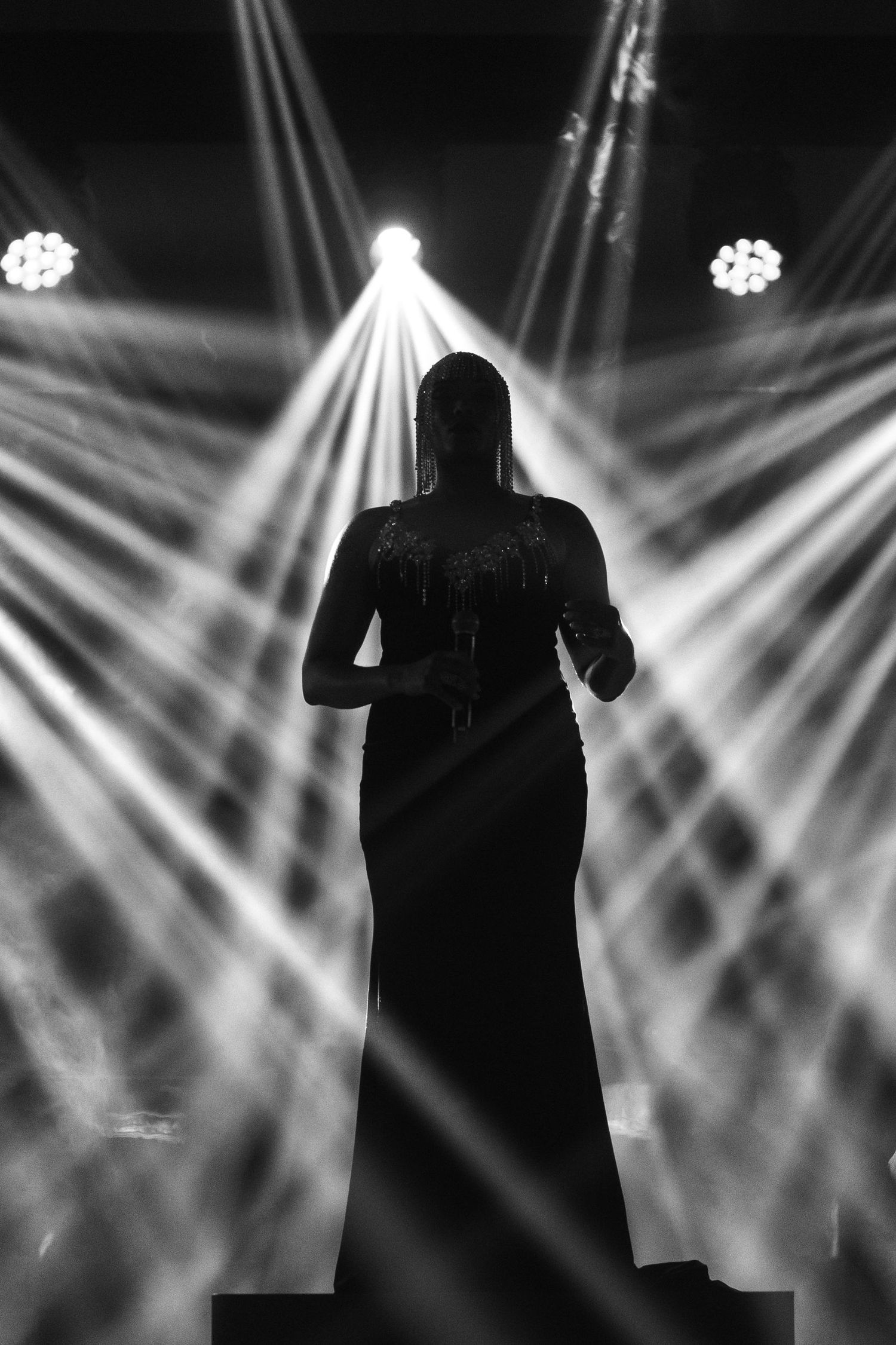 Dramatic silhouette of a performer on stage with crisscrossing white spotlight beams.
