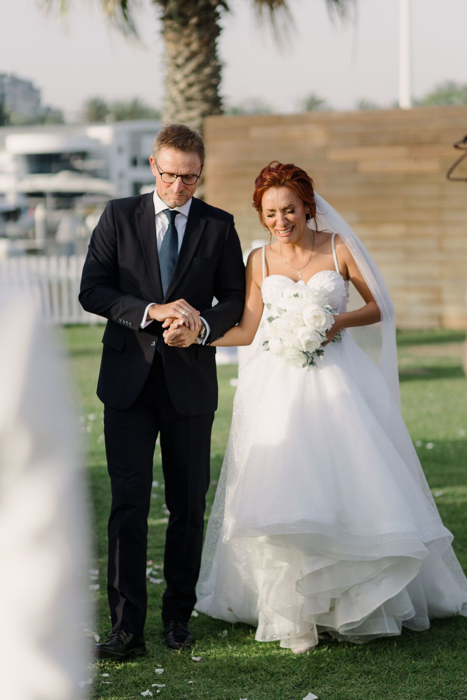 Couple sharing playful moment on grassy lawn during wedding photoshoot.