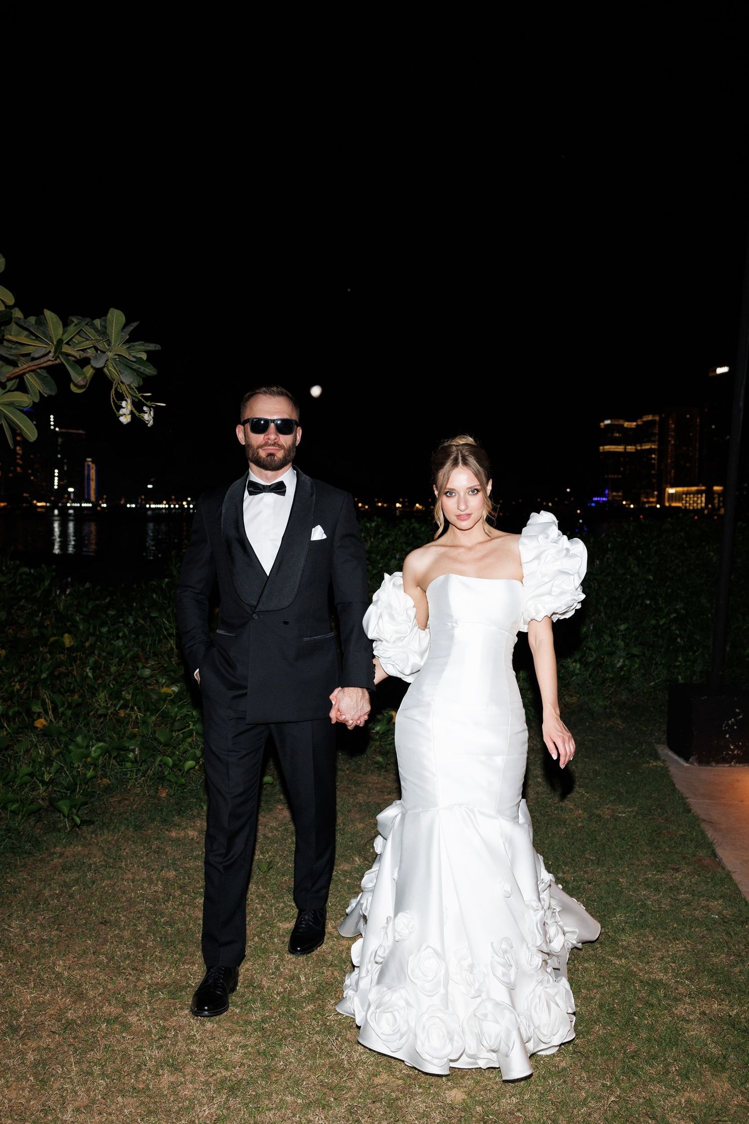 Wedding couple walking together on grass during evening celebration.