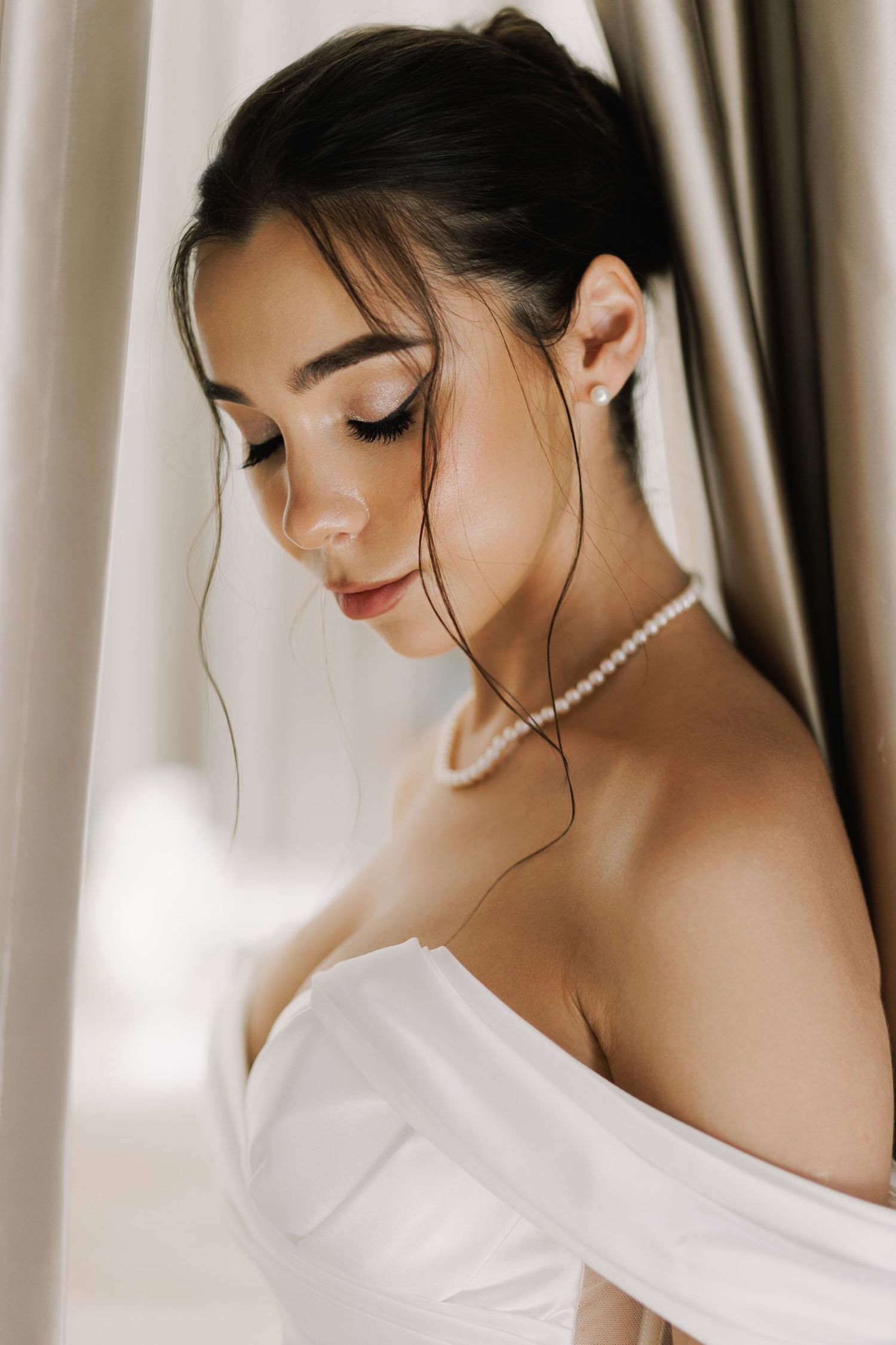 Side profile portrait in soft lighting wearing pearl necklace and white dress.