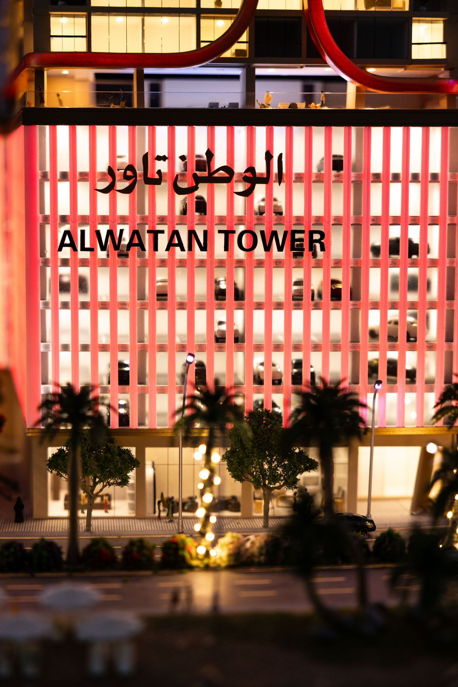 Illuminated exterior of Alwatan Tower at night with modern architectural lighting and palm trees in the foreground.