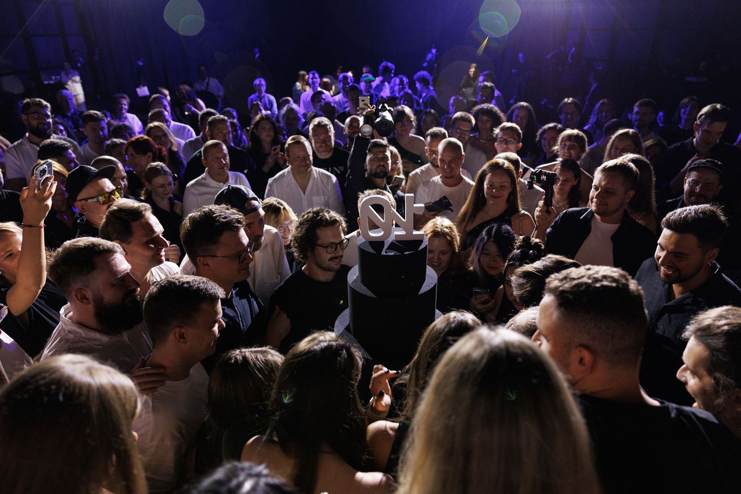Crowded audience watches performance in dimly lit venue.