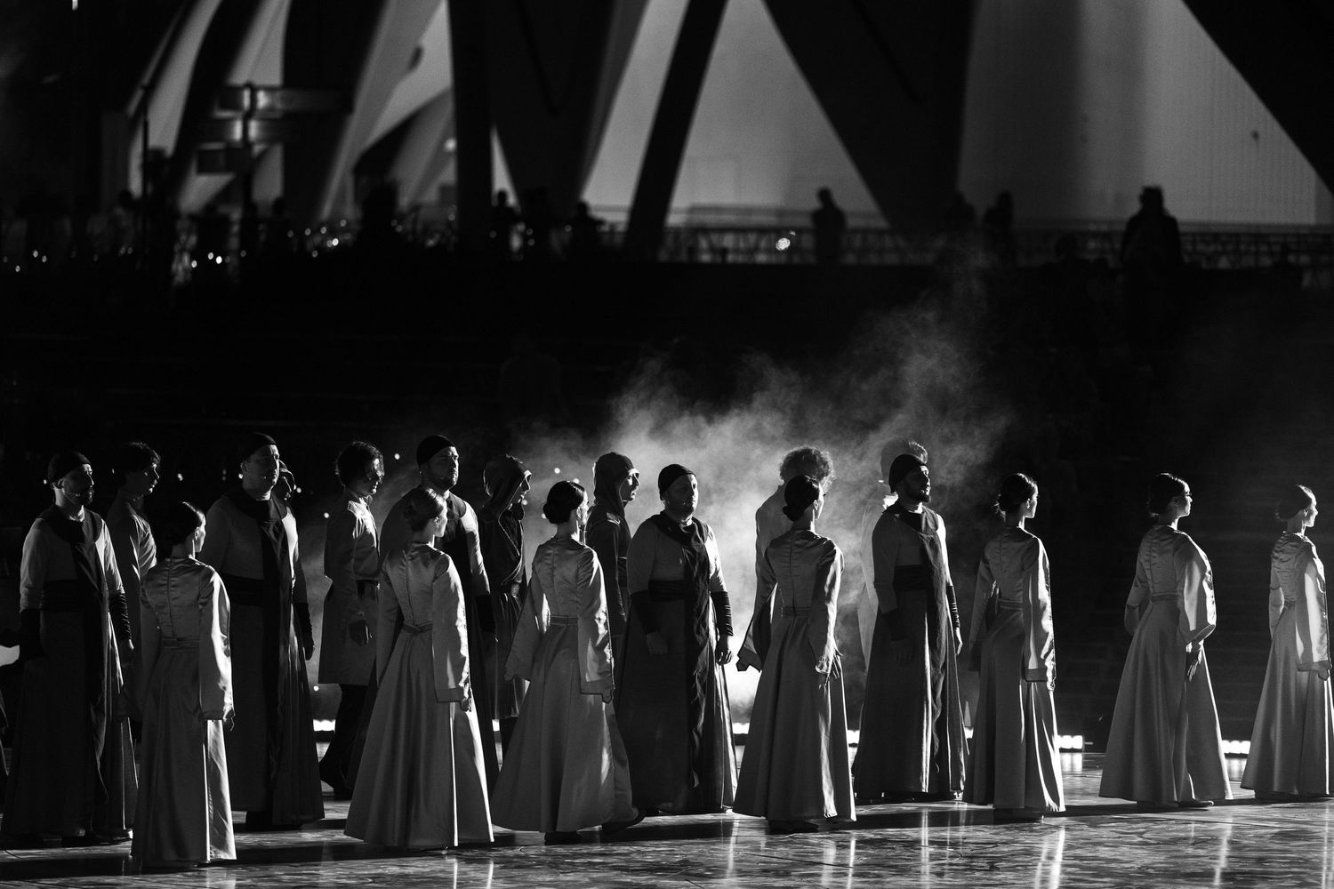 Performers lined up in silhouette on a darkened stage during a theatrical production.