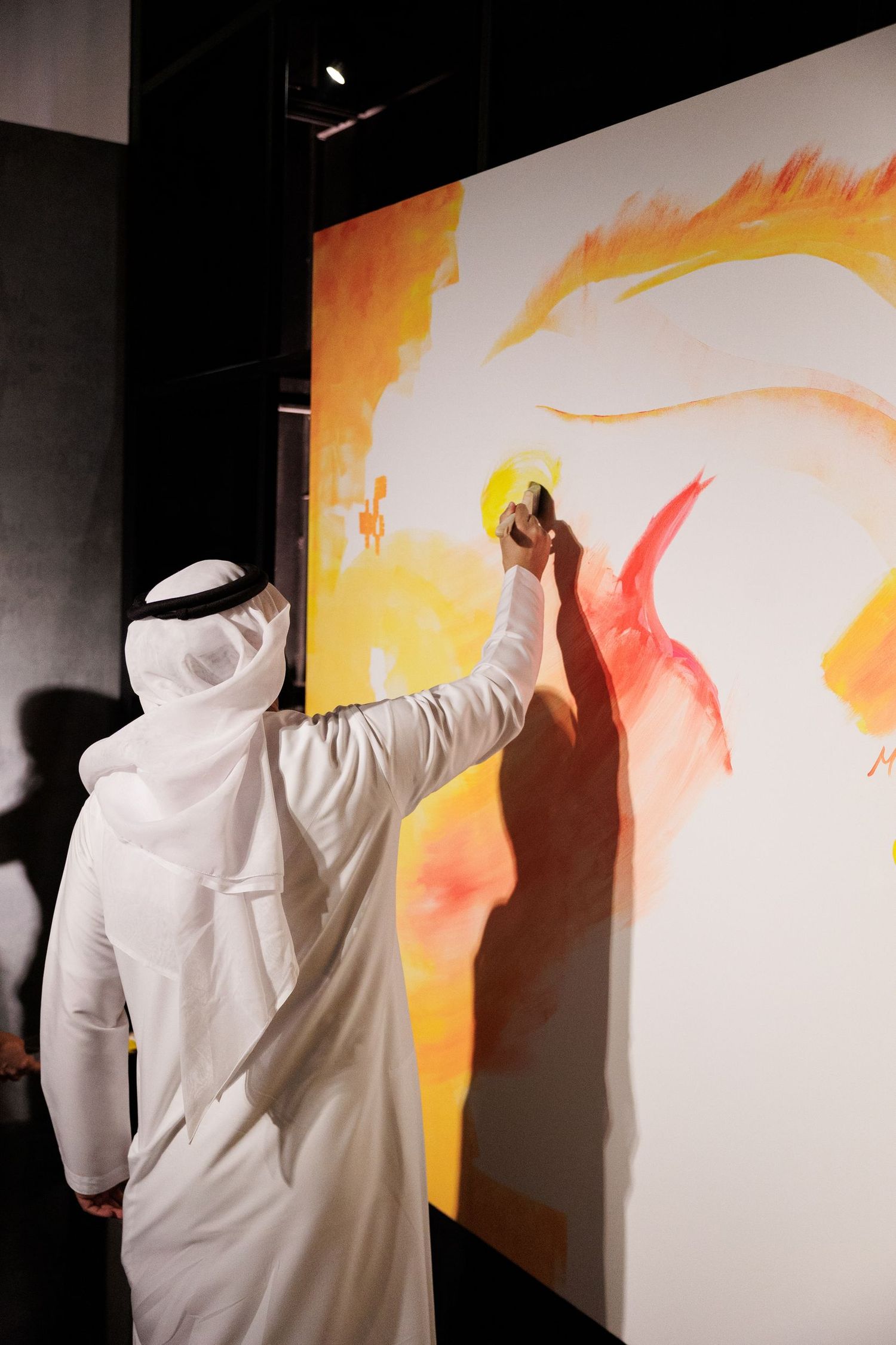 Person in traditional Middle Eastern dress painting on a large canvas with orange and yellow hues.