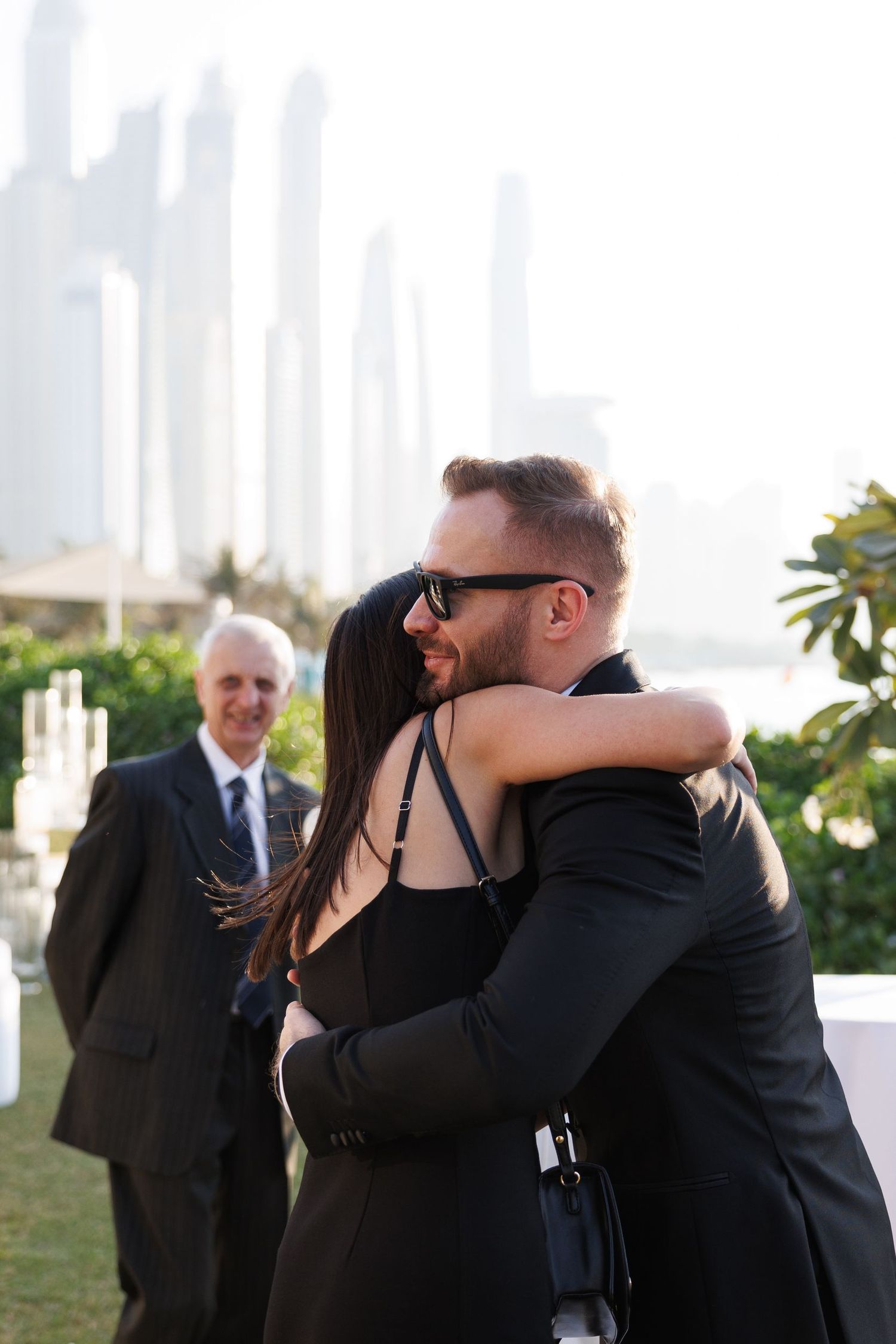 Wedding party members embrace and celebrate during an outdoor ceremony with city views.