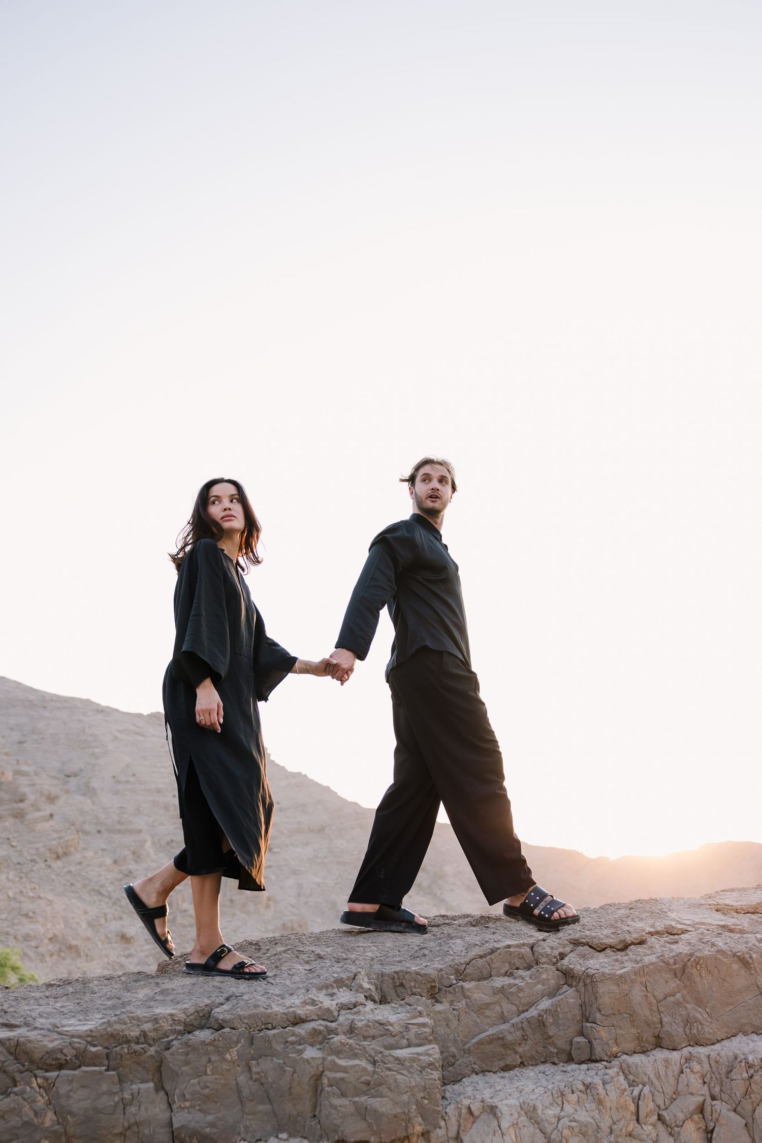 A couple holding hands while exploring rocky terrain against a bright sky.