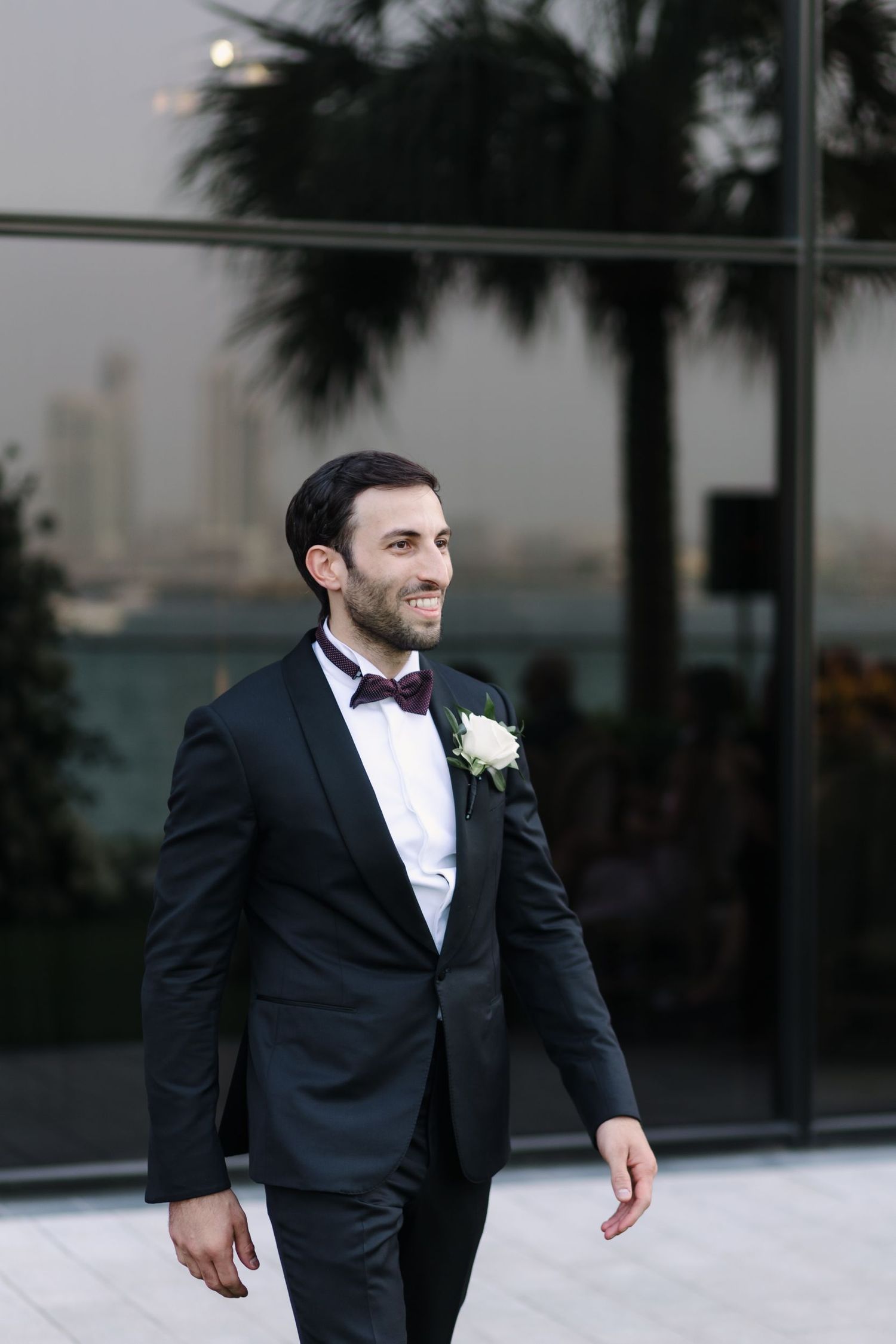 A groom in a classic black tuxedo and bow tie poses during wedding photos.