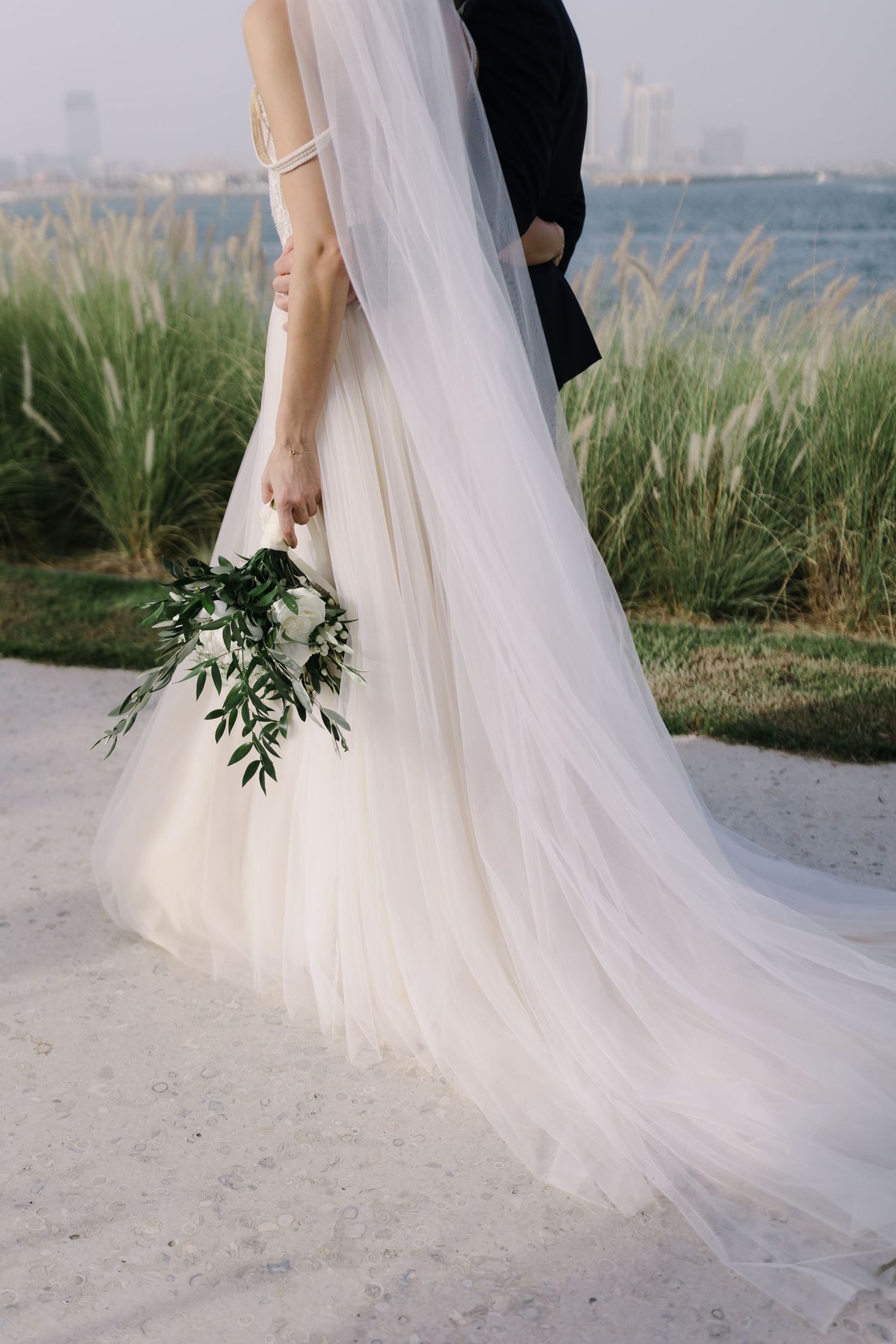 Flowing white wedding dress train photographed against coastal landscape.