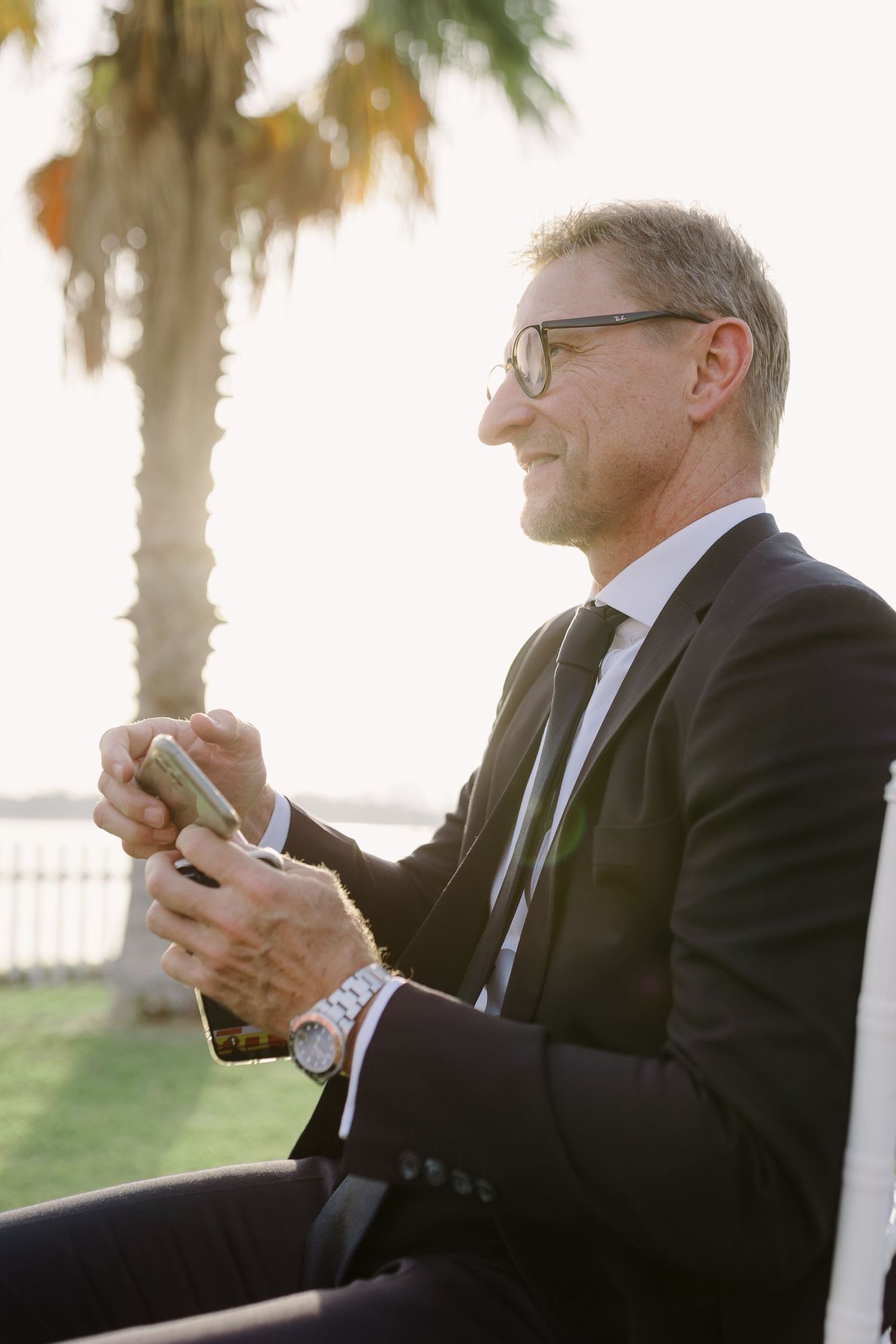 Wedding guests in formal attire using mobile phones at an outdoor reception.
