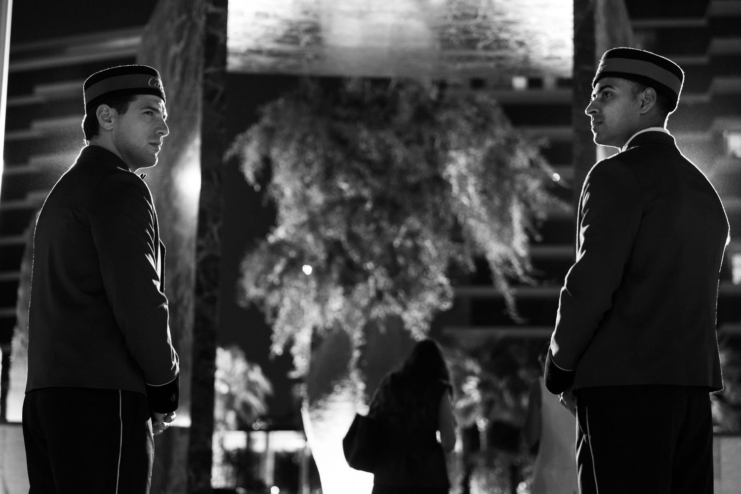 A black and white film noir style collage of people in dark coats and hats standing in atmospheric lighting.