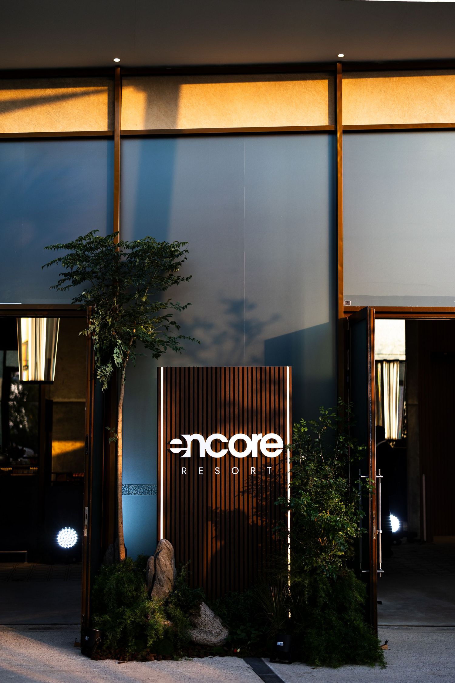 Modern restaurant entrance with illuminated 'encore' signage and glass walls at dusk creates an elegant atmosphere.