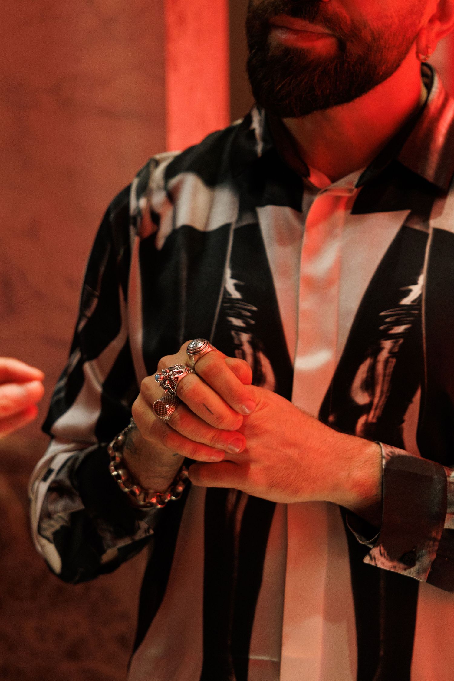 Hands wearing rings and bracelets gesturing against a red-tinted background.