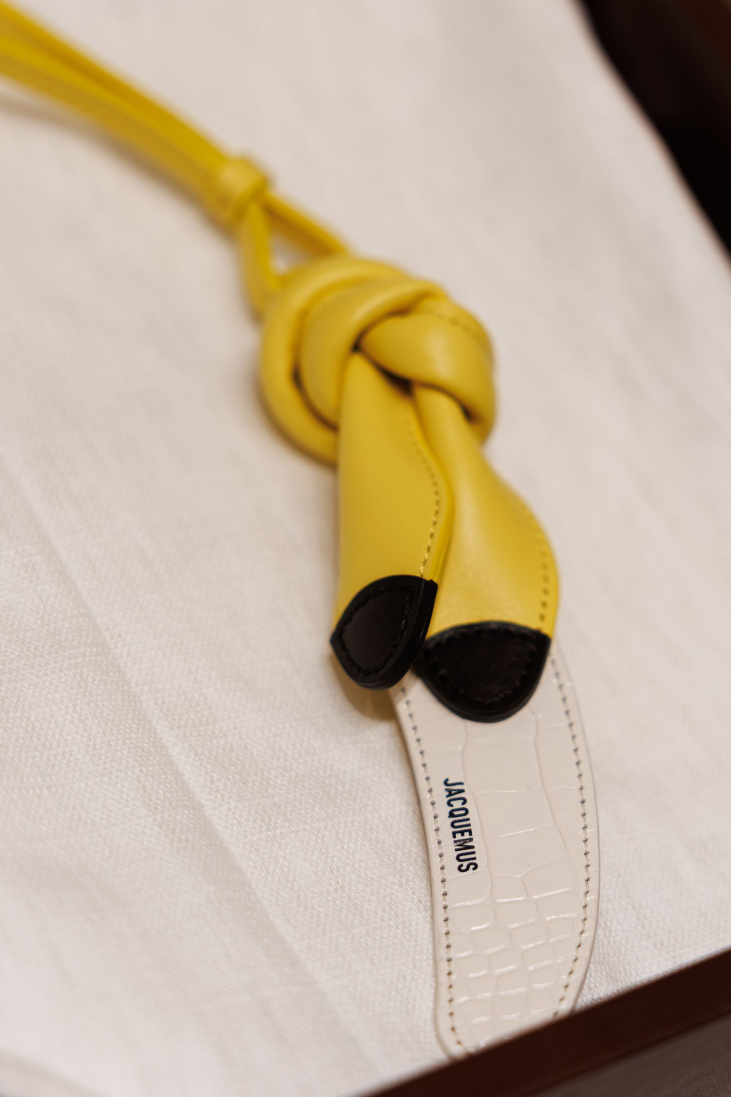 Yellow leather knotted accessory with black tips on white fabric.
