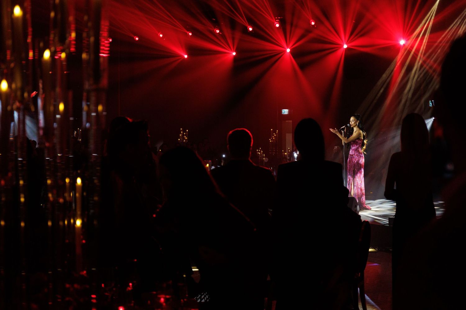 Red concert lighting creates dramatic rays and patterns across a dark venue.