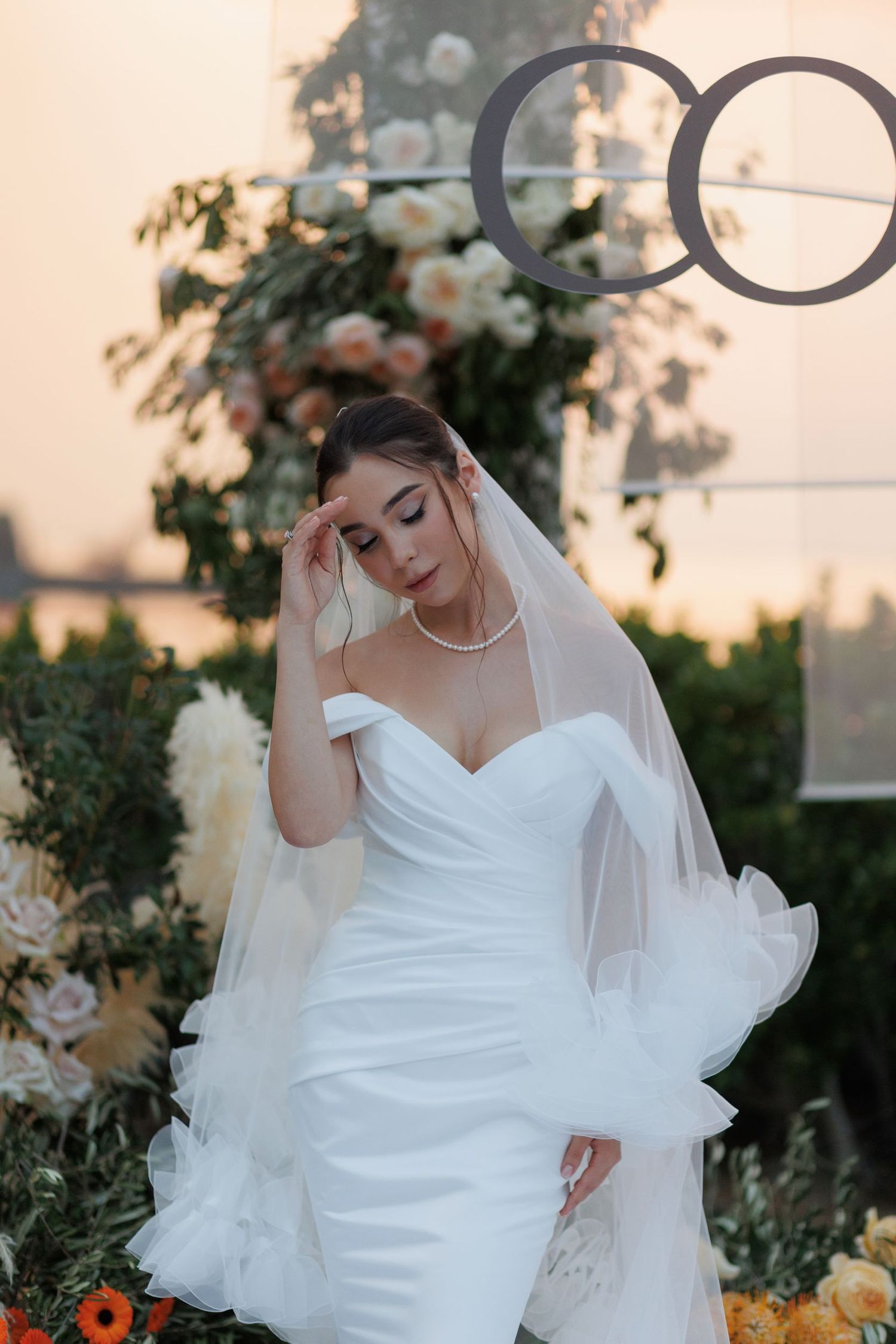 A bride in a white wedding dress poses gracefully during sunset in an outdoor garden setting.