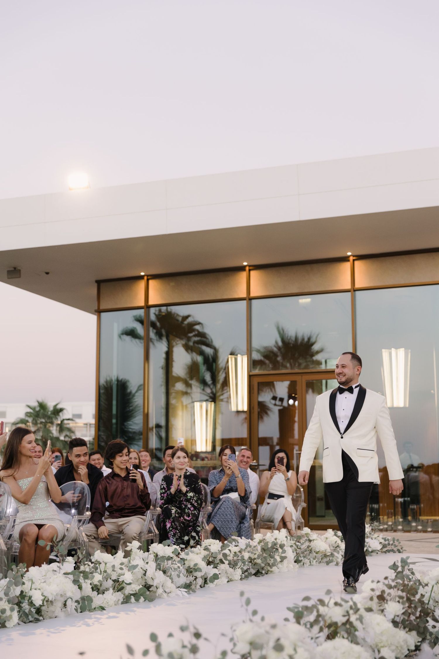 Elegant outdoor wedding runway with white floral decorations and modern architecture.