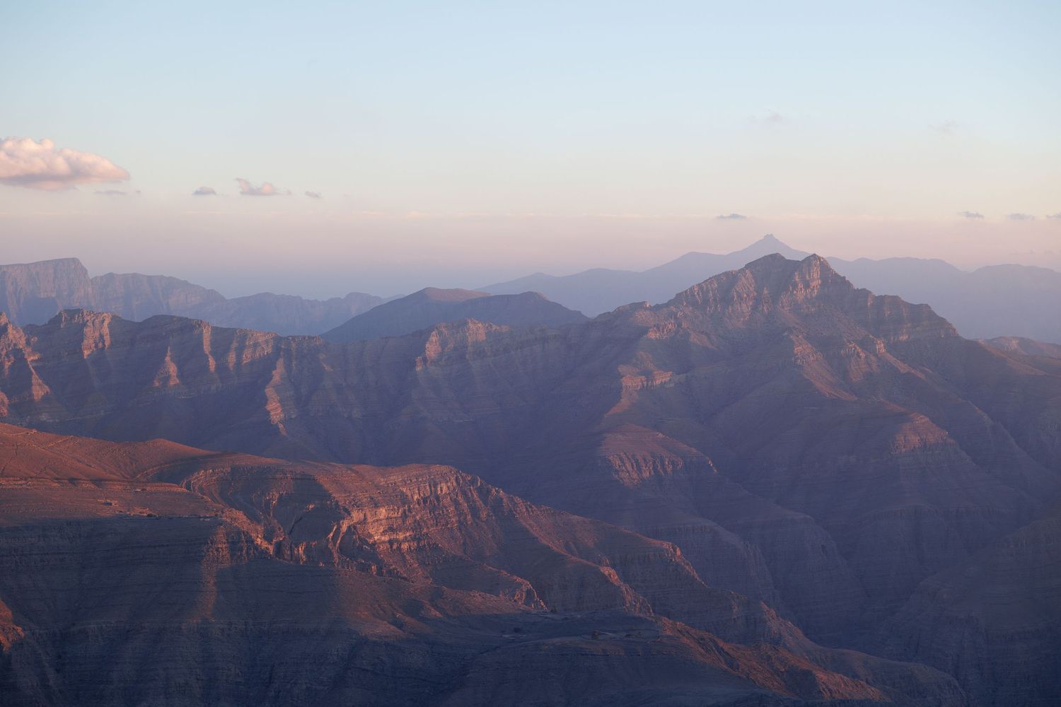 Panoramic view of mountain ranges during sunset with layered peaks extending into the distance.
