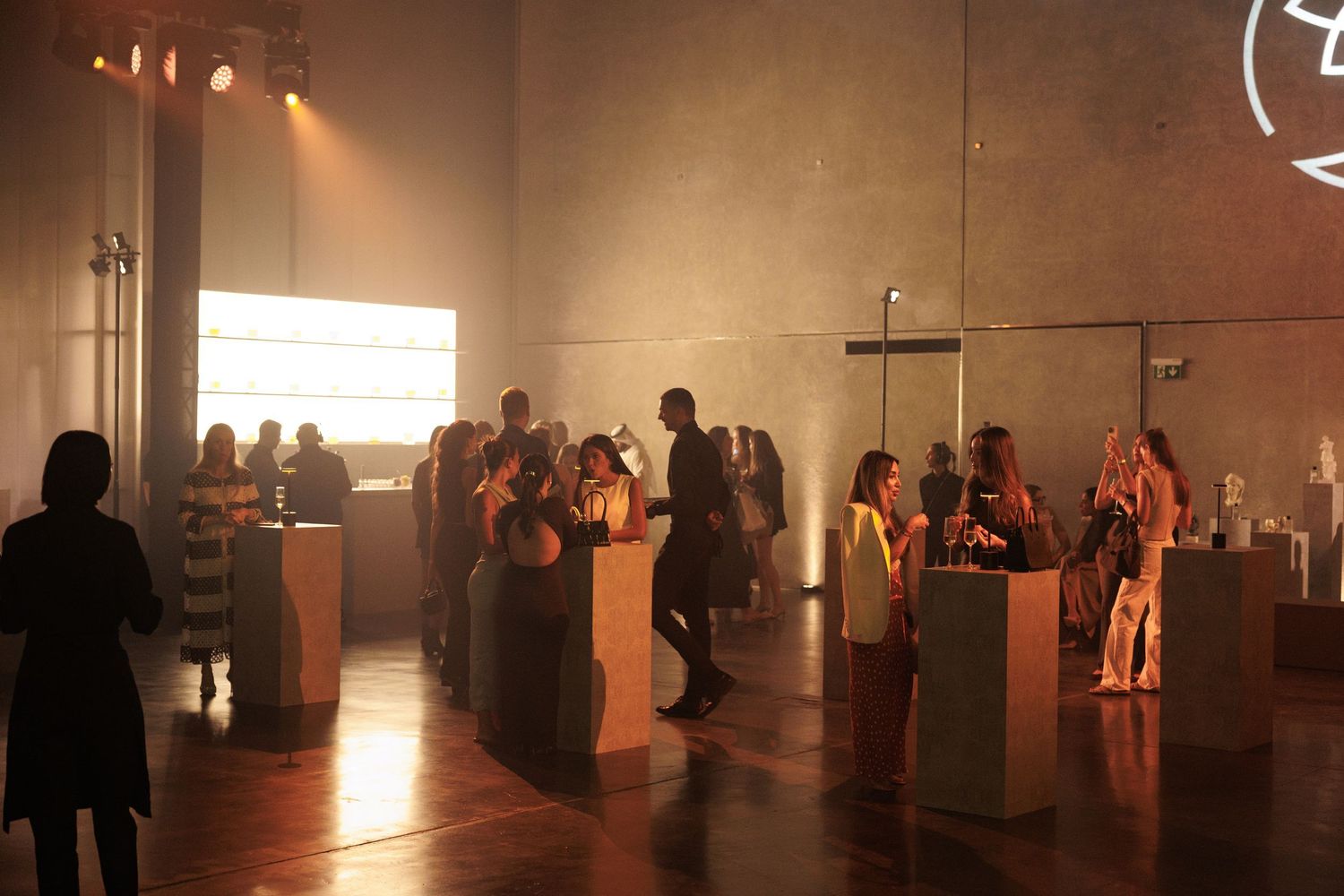 Dimly lit gallery space with silhouettes of people viewing art installations.