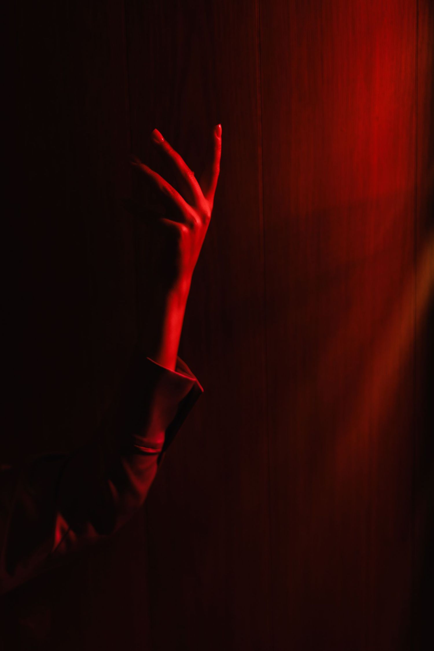 Artistic shot of a hand reaching upward in dramatic red lighting.