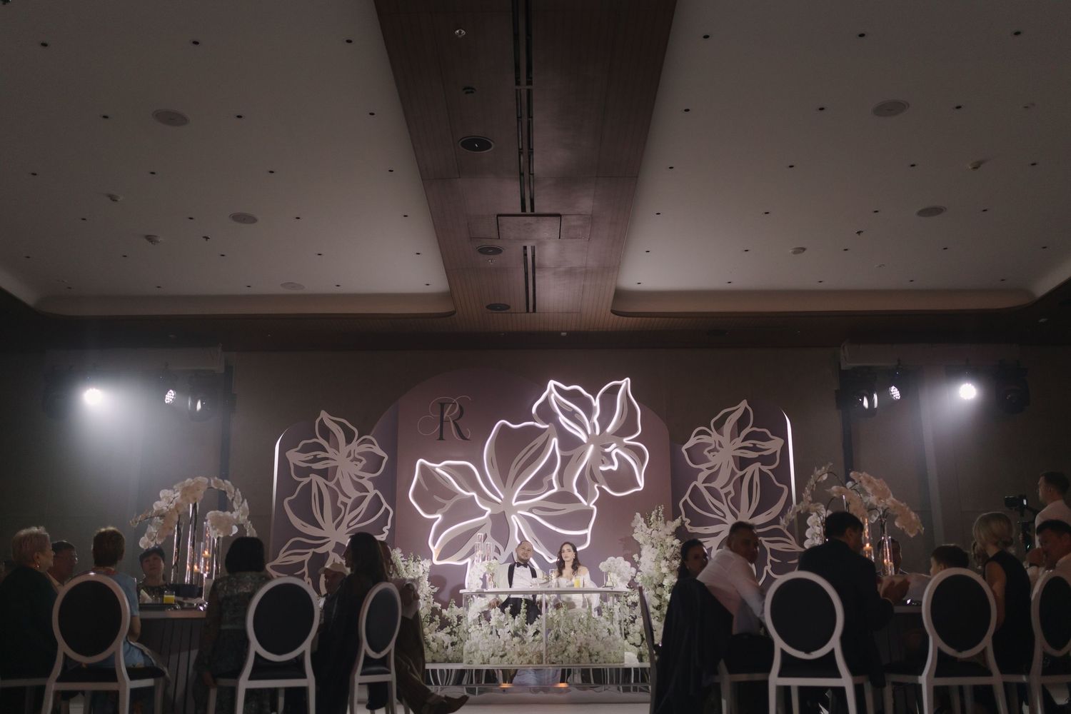 Wide shot of an elegant wedding reception hall with illuminated floral wall designs.
