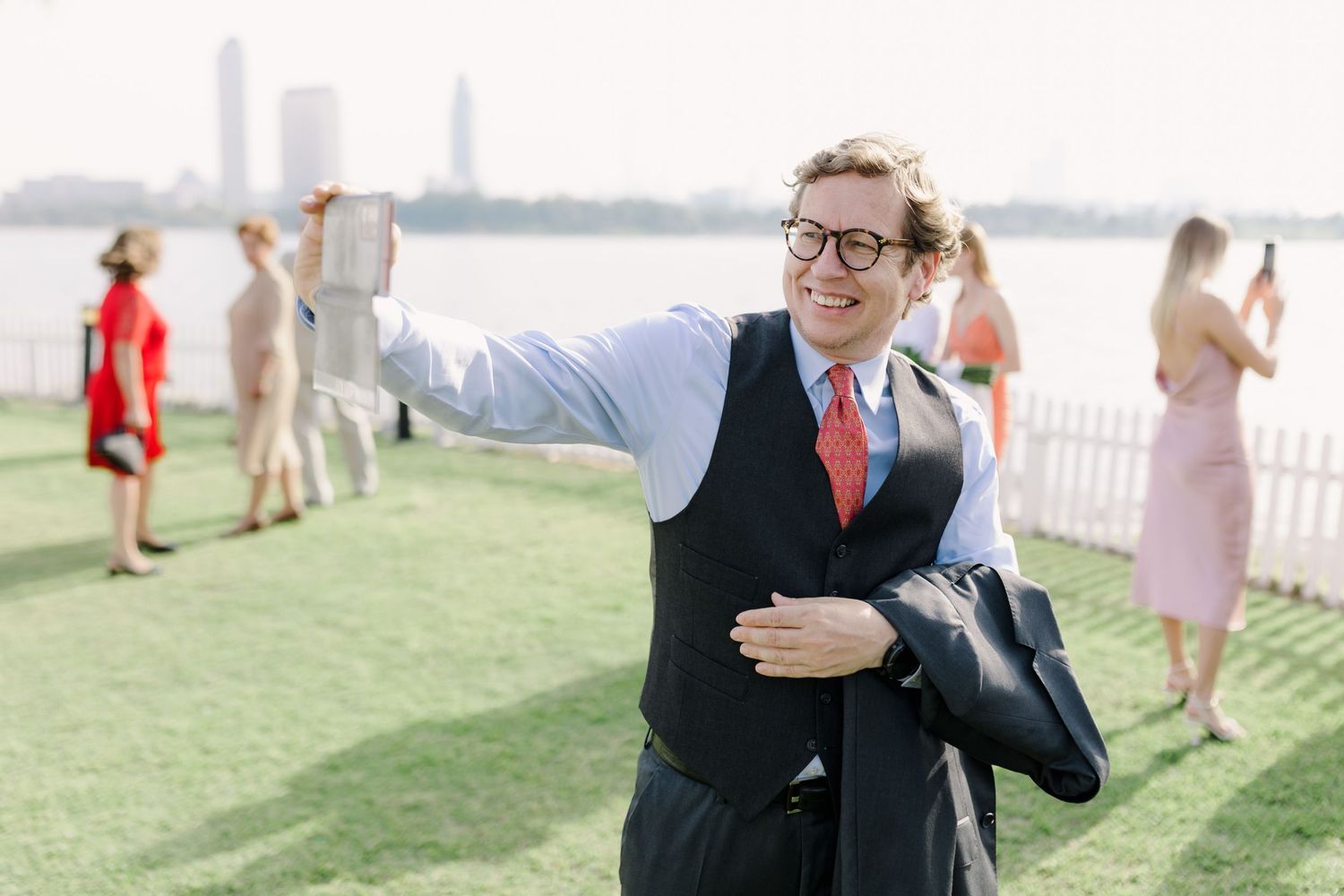 Wedding guests celebrating on a grassy lawn with a waterfront view.