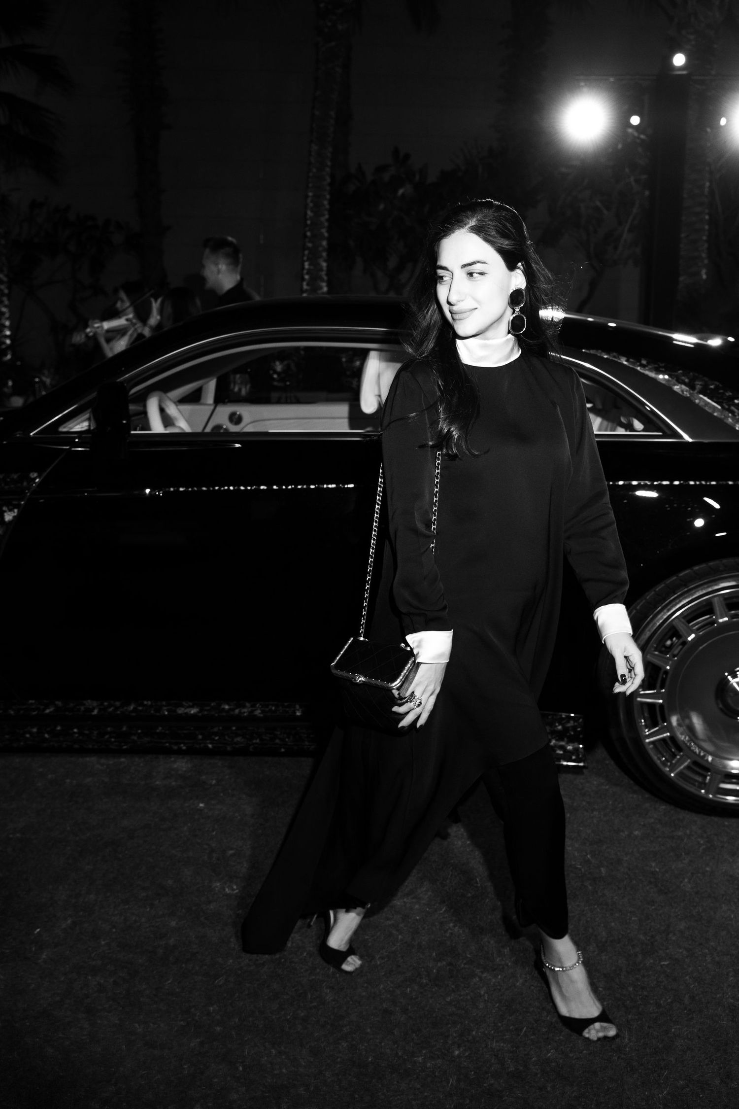 A person in black clothing walks at night near parked cars.