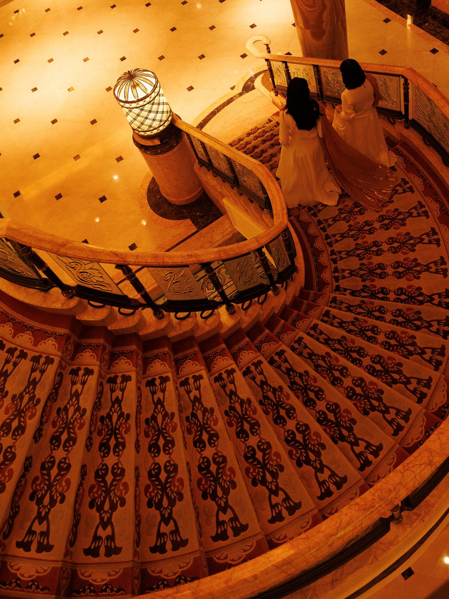 Spiral staircase with ornate wrought iron railings illuminated by warm lighting creates dramatic shadows and patterns.