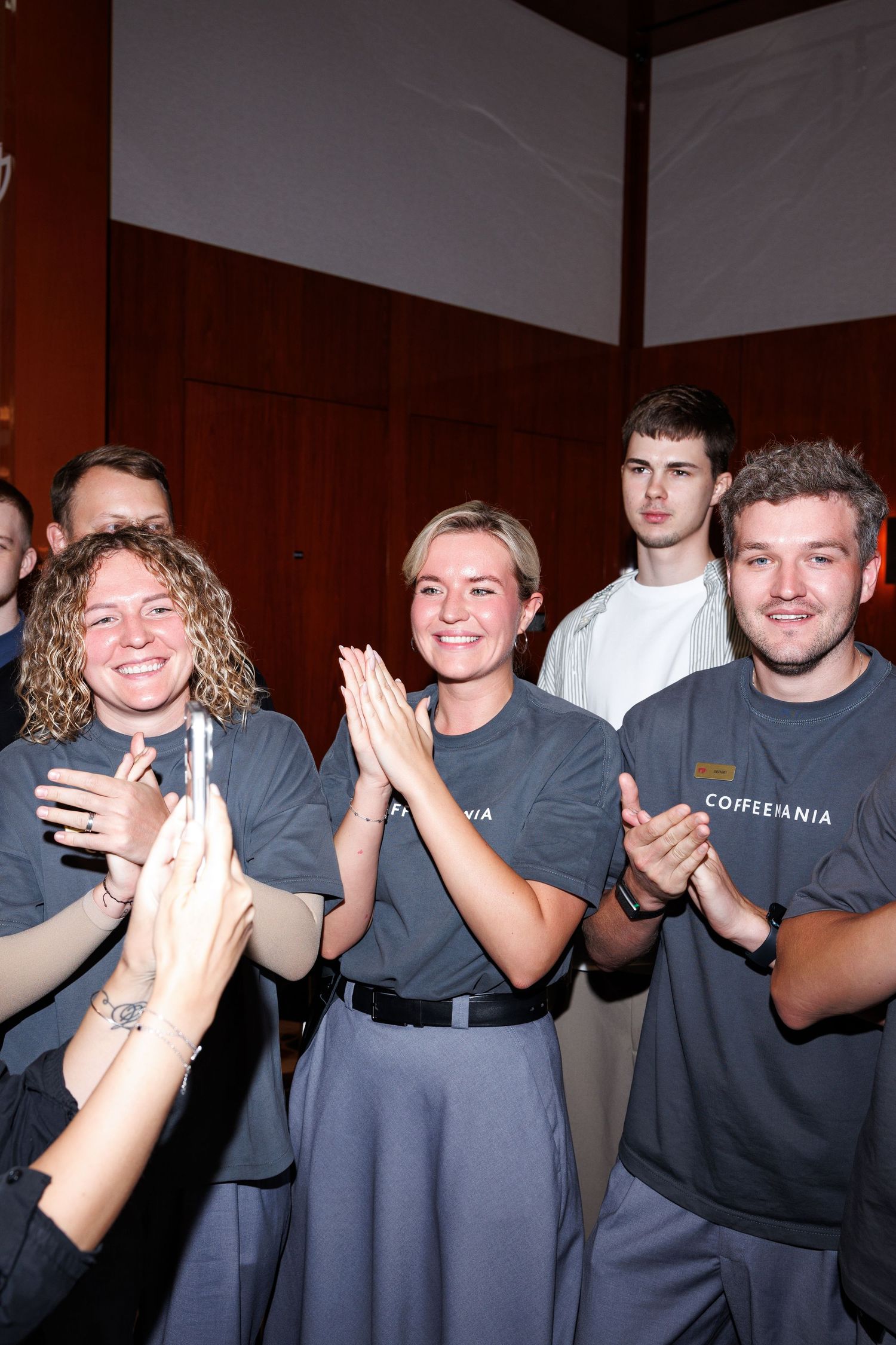 Staff members in grey uniforms applauding during company event.