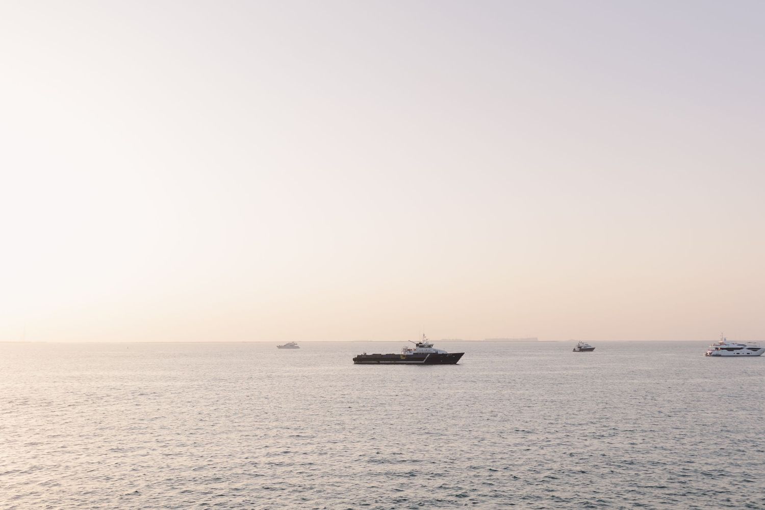 Boats floating on calm waters during sunset with a misty horizon.