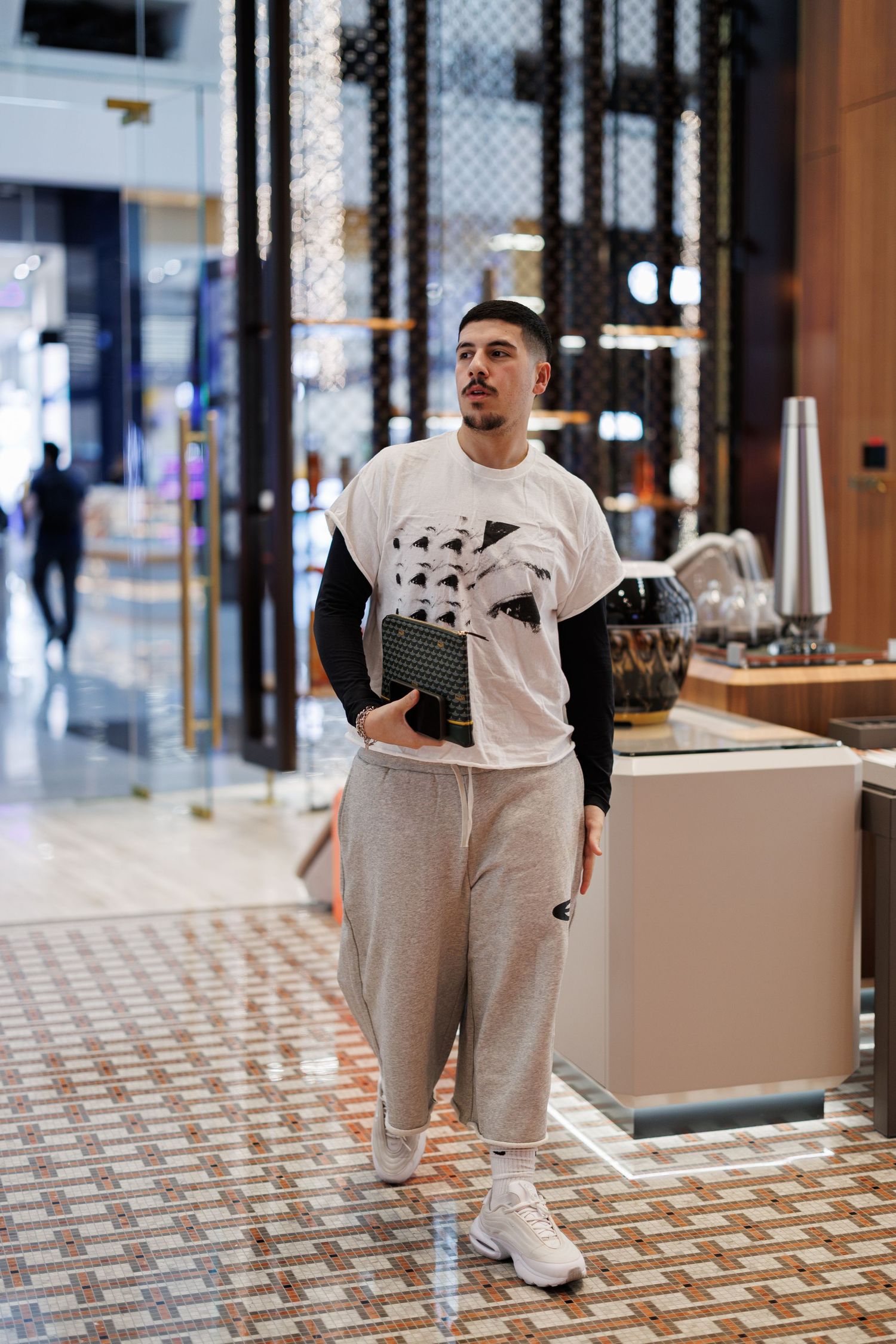 Person wearing casual white and gray outfit standing in modern retail space with tiled floor.